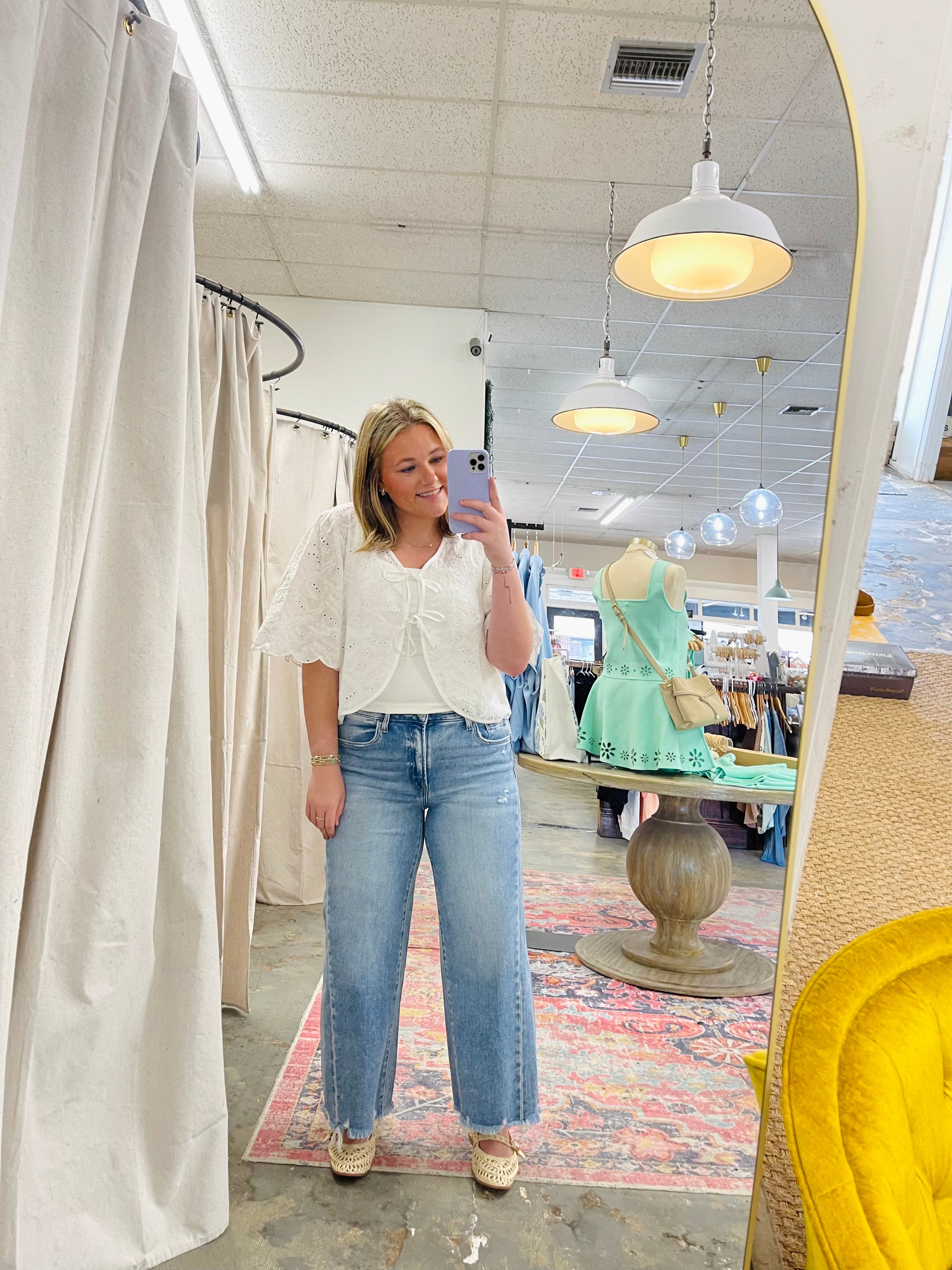 Woman wearing white eyelet Hazel top with puffed sleeves and blue jeans in clothing store dressing room