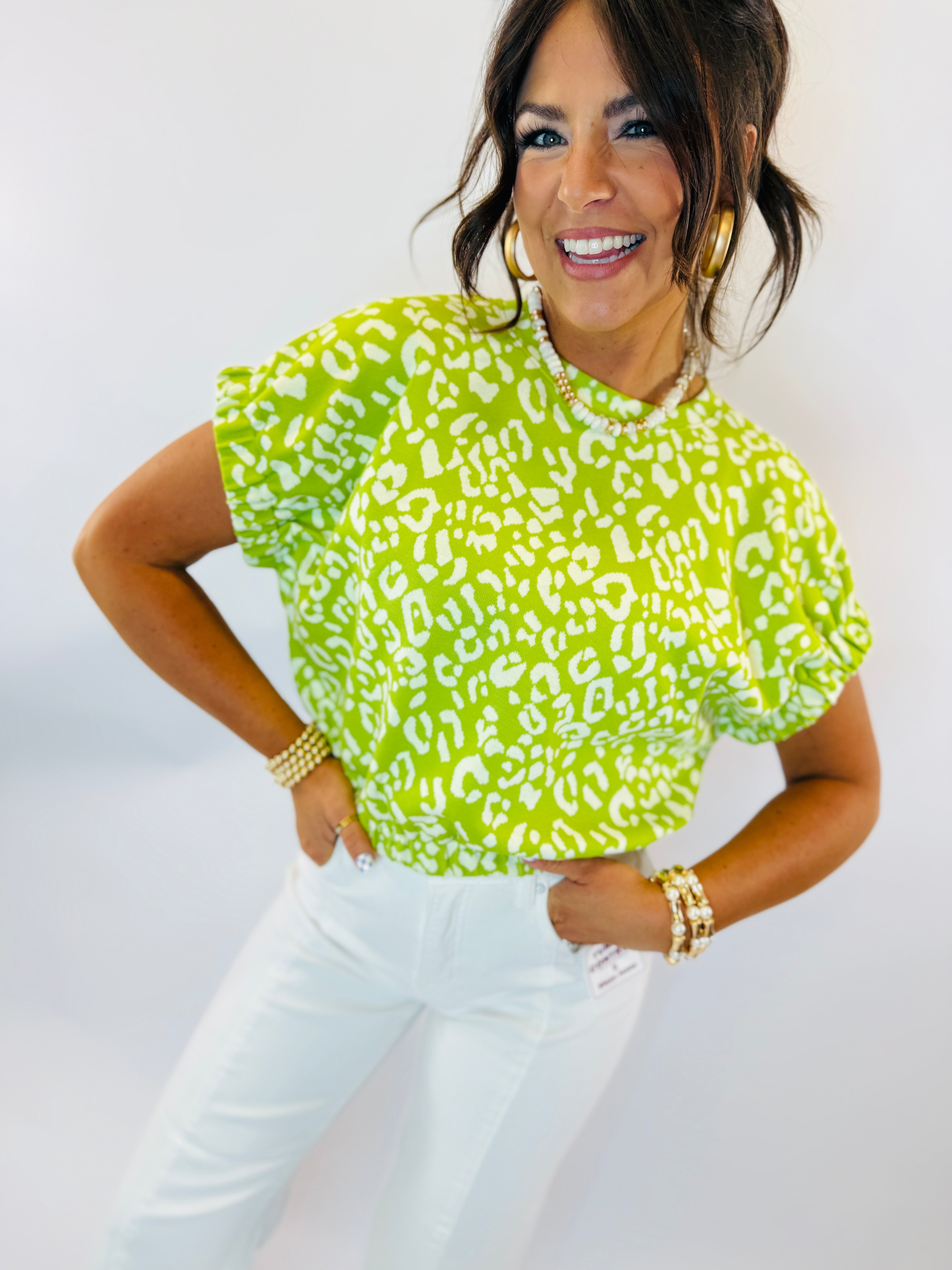 Woman wearing bright green leopard print Tally Top with white pants and gold jewelry accessories.