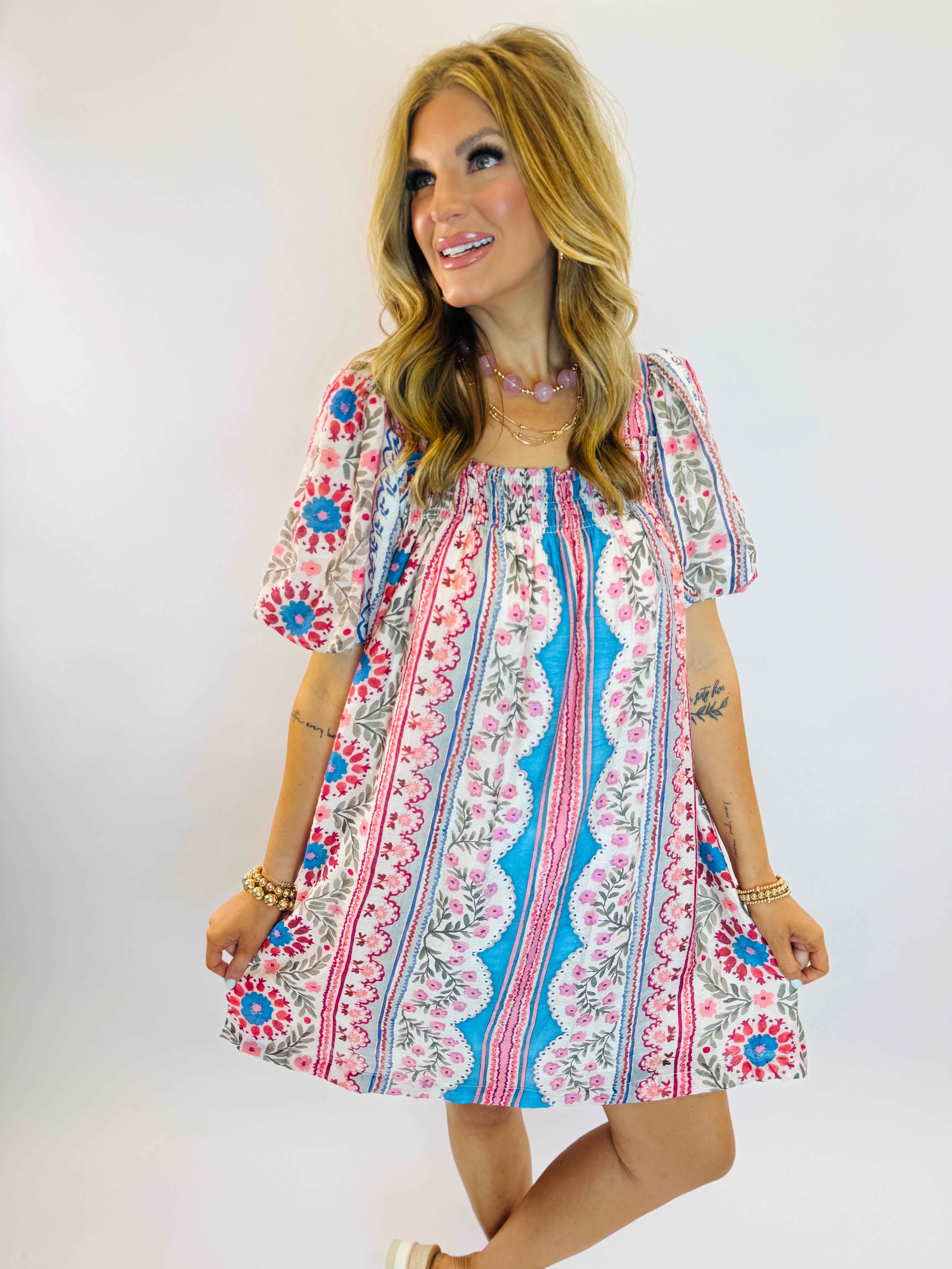 Woman wearing colorful floral patterned short-sleeve dress with blue, pink, and white bohemian print design