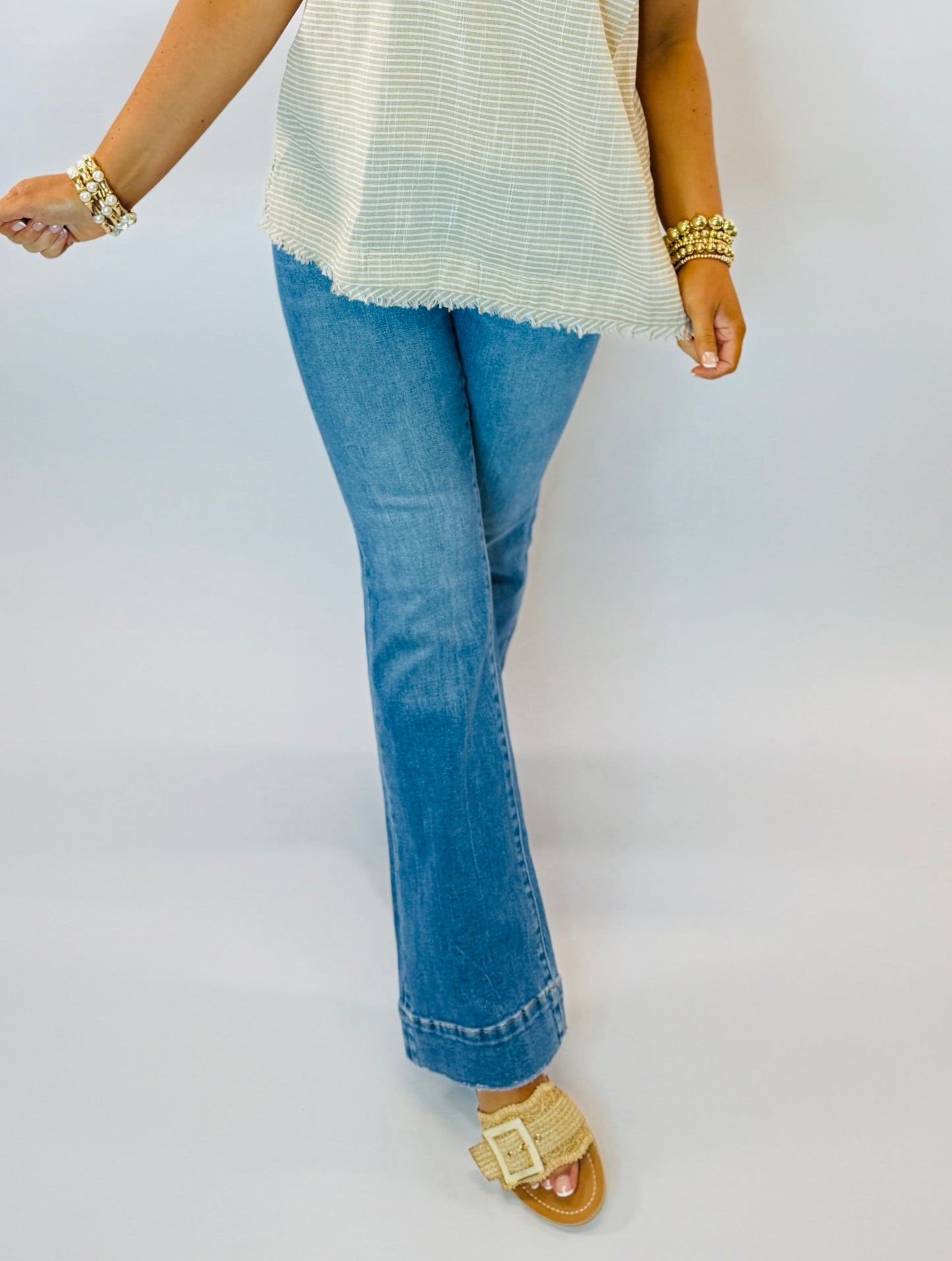 Woman wearing cream striped sleeveless top with frayed hem, blue jeans, and gold jewelry accessories