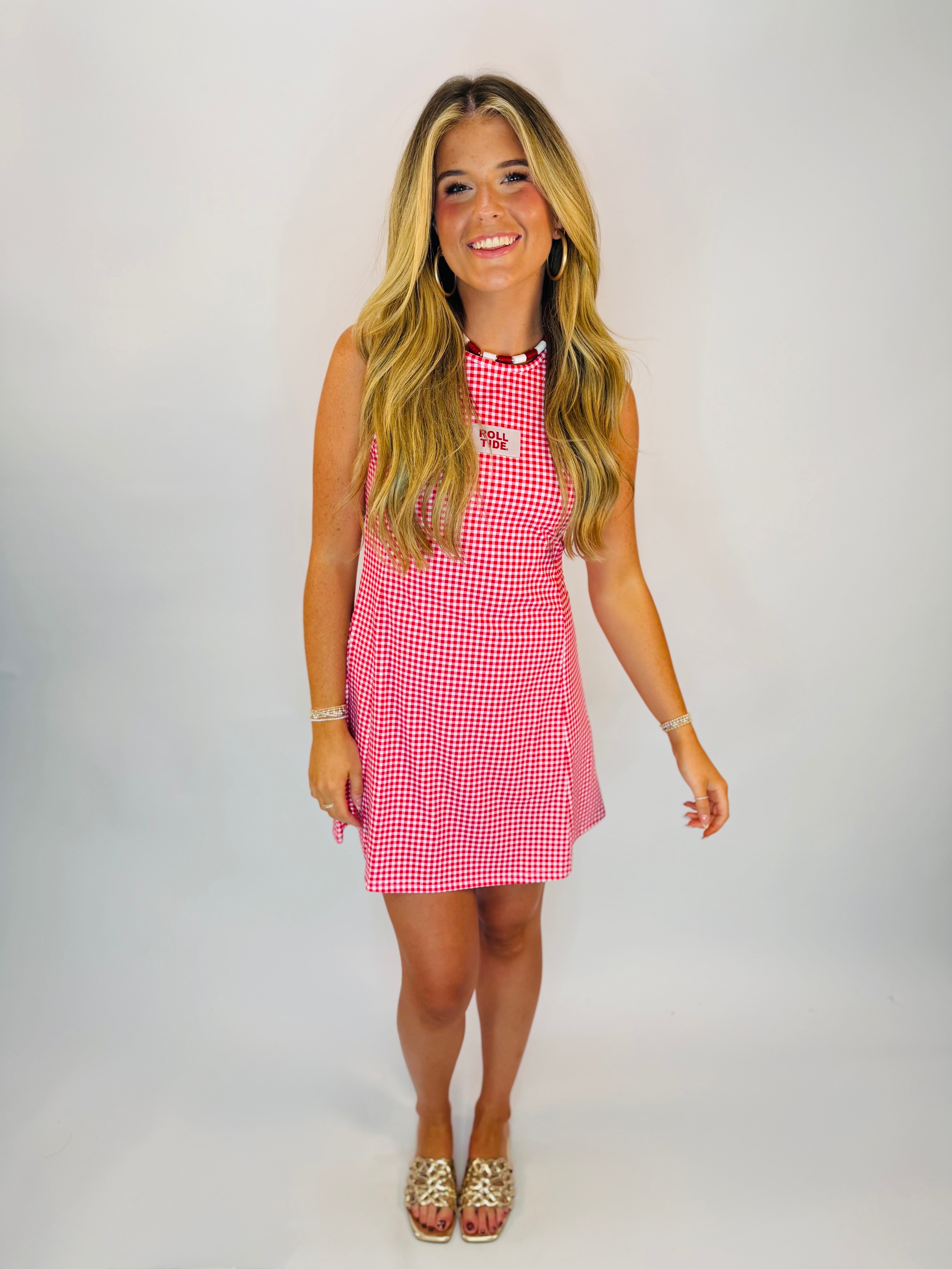 Red and white gingham sleeveless mini dress with "Roll Tide" patch, worn with gold sandals.