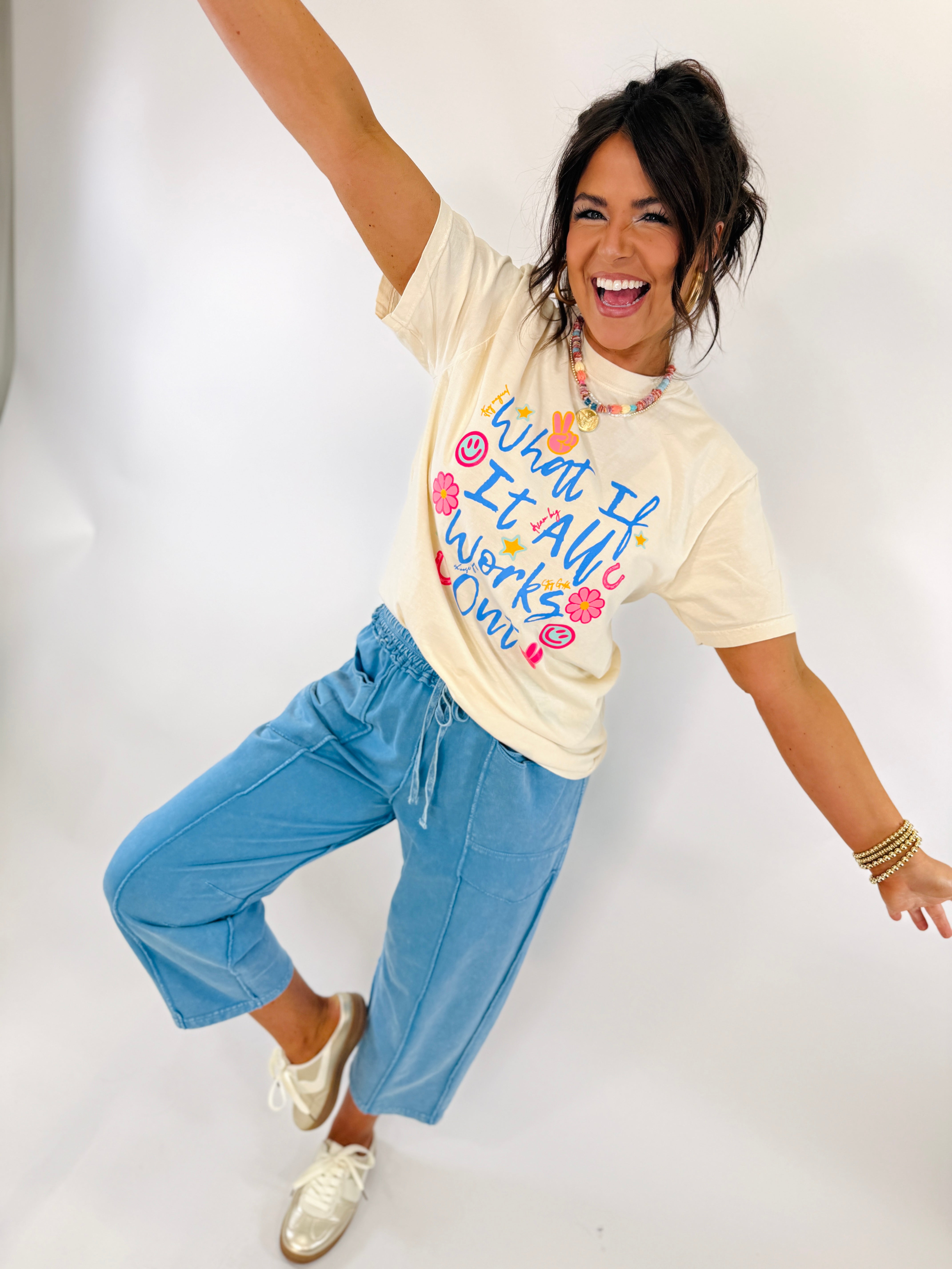 Woman wearing blue wide leg sweatpants with drawstring waist, paired with cream graphic tee and sneakers.