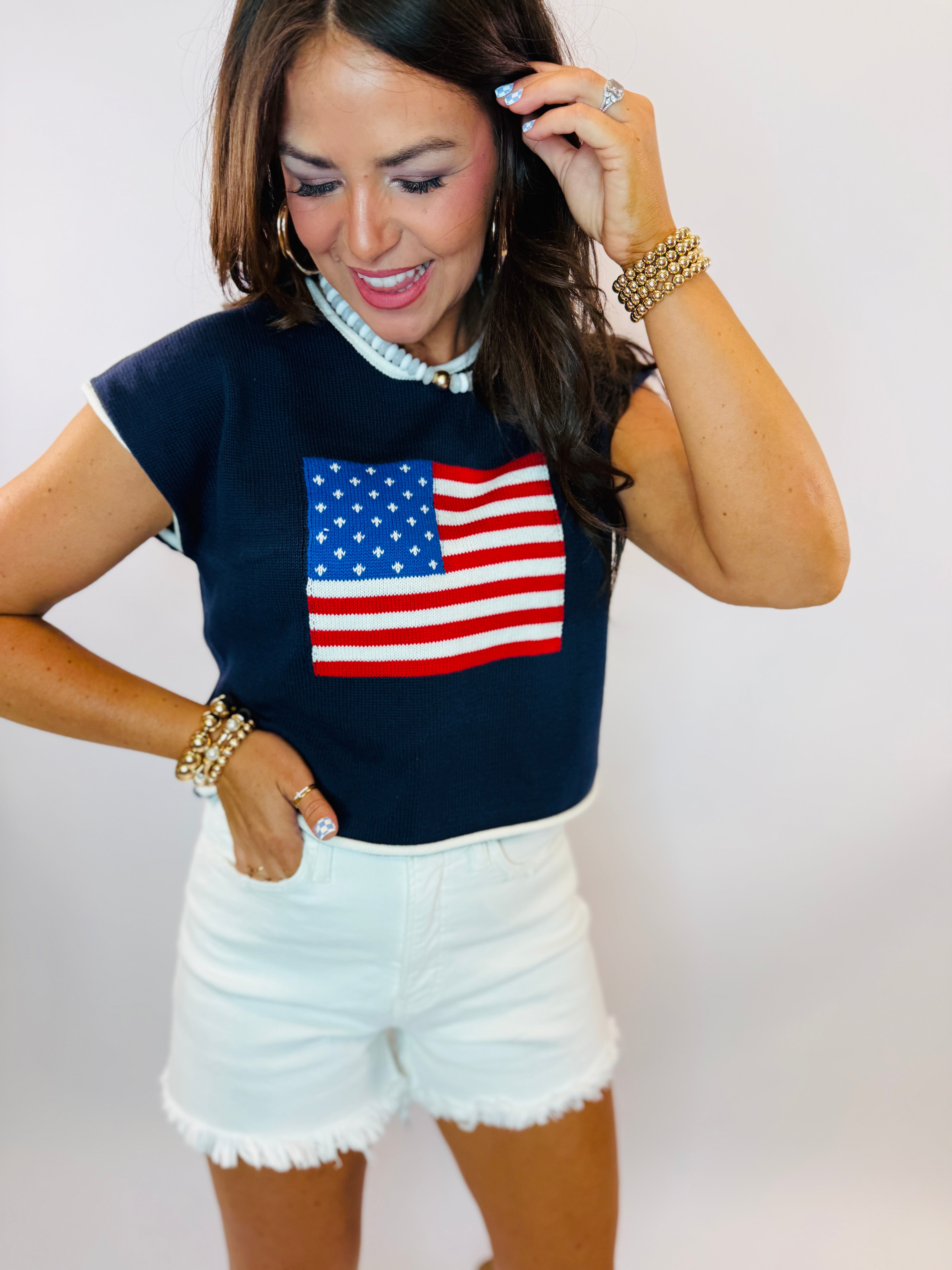 Navy knit top with American flag design, short sleeves, worn with white denim shorts and pearl accessories.