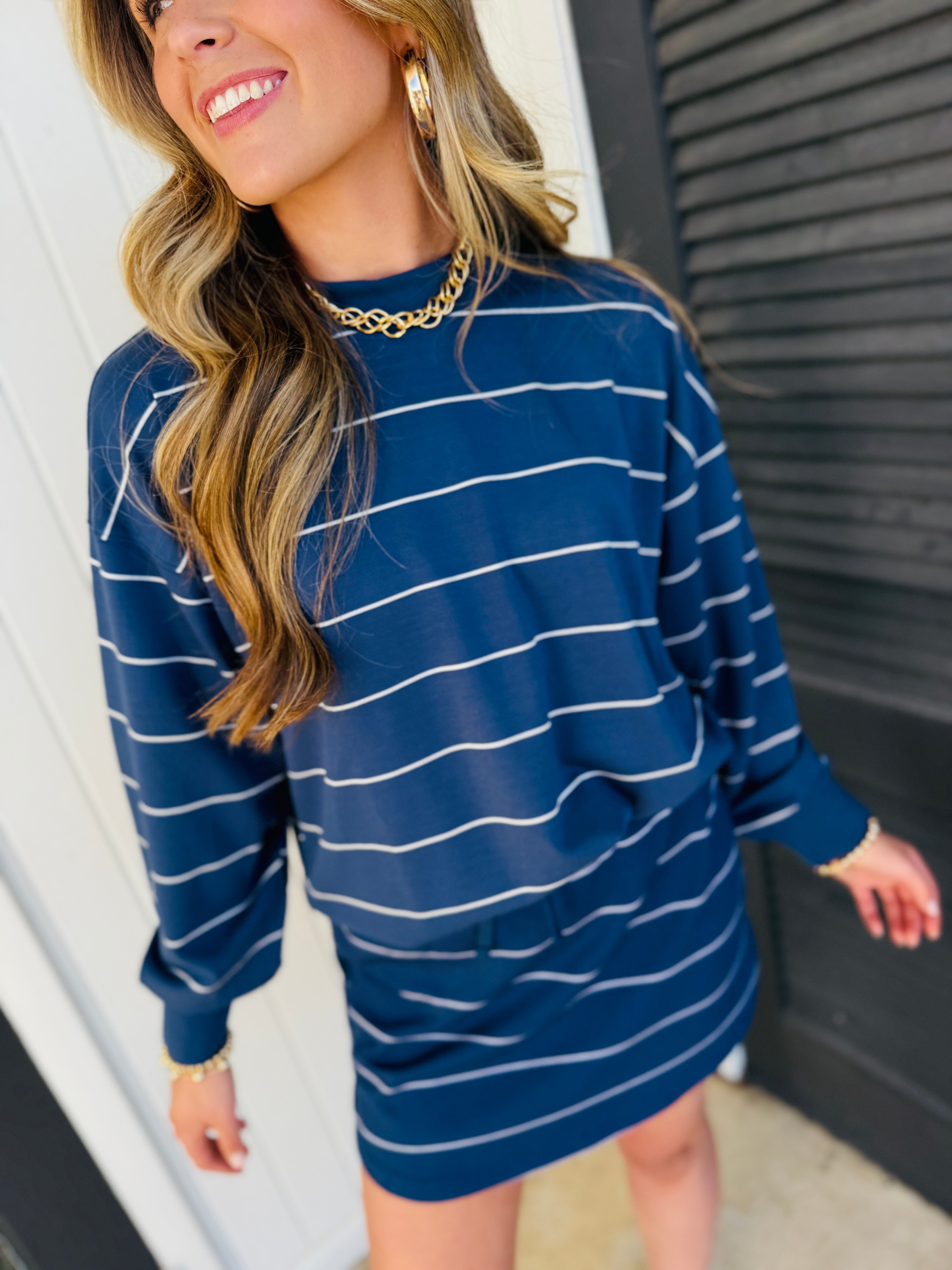 Woman wearing blue and white striped oversized sweatshirt with gold chain necklace and hoop earrings.