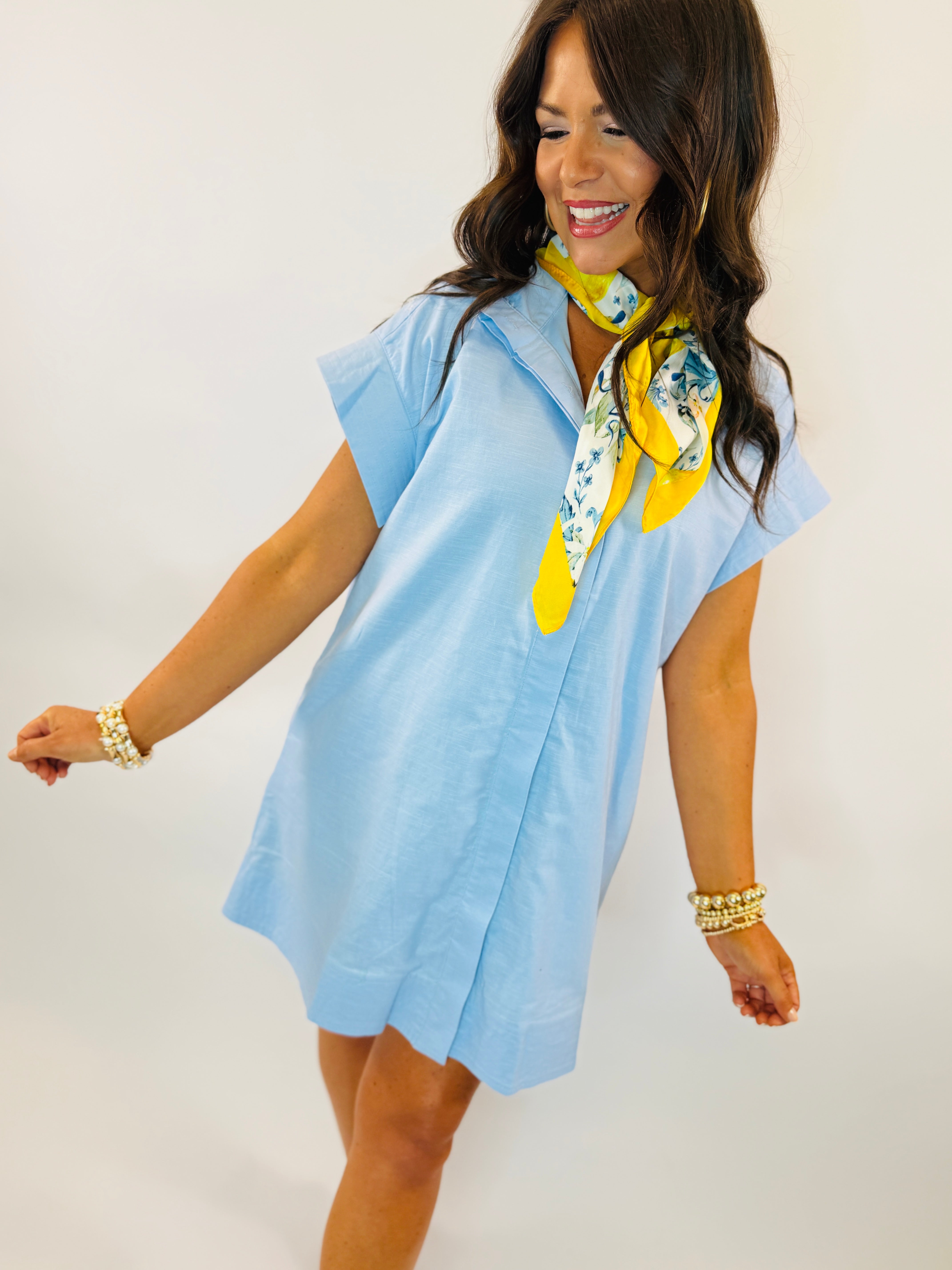 Woman wearing light blue short-sleeve Penelope dress with yellow floral scarf and pearl bracelets against white background.