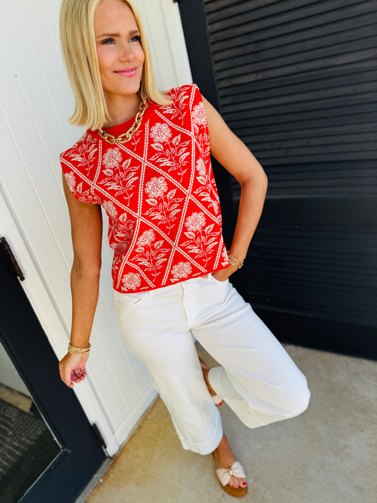 Woman wearing red floral patterned Lola Meadow soft top with white pants and gold jewelry accessories