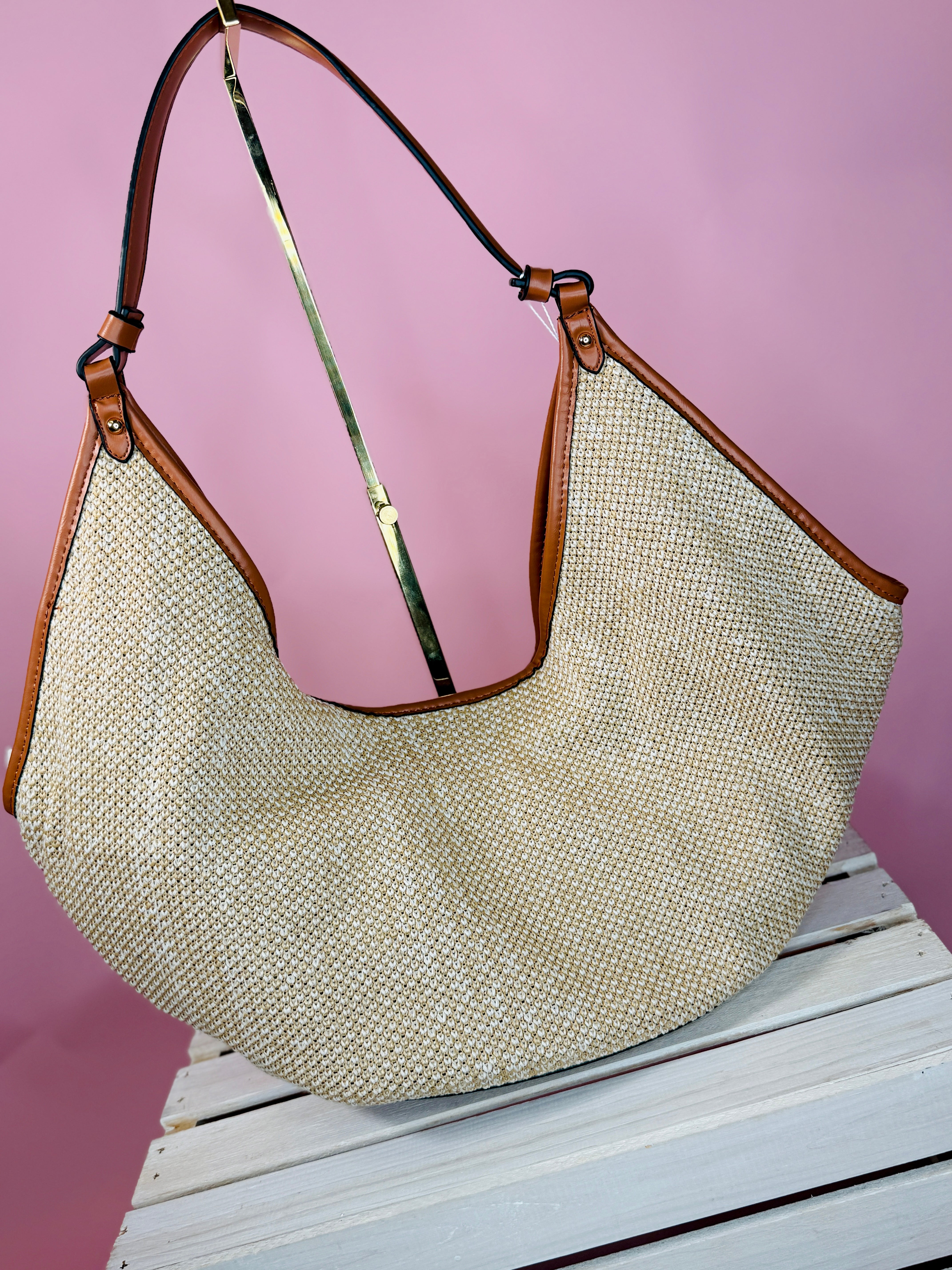 Large woven tote bag with brown leather trim and adjustable strap on wooden surface