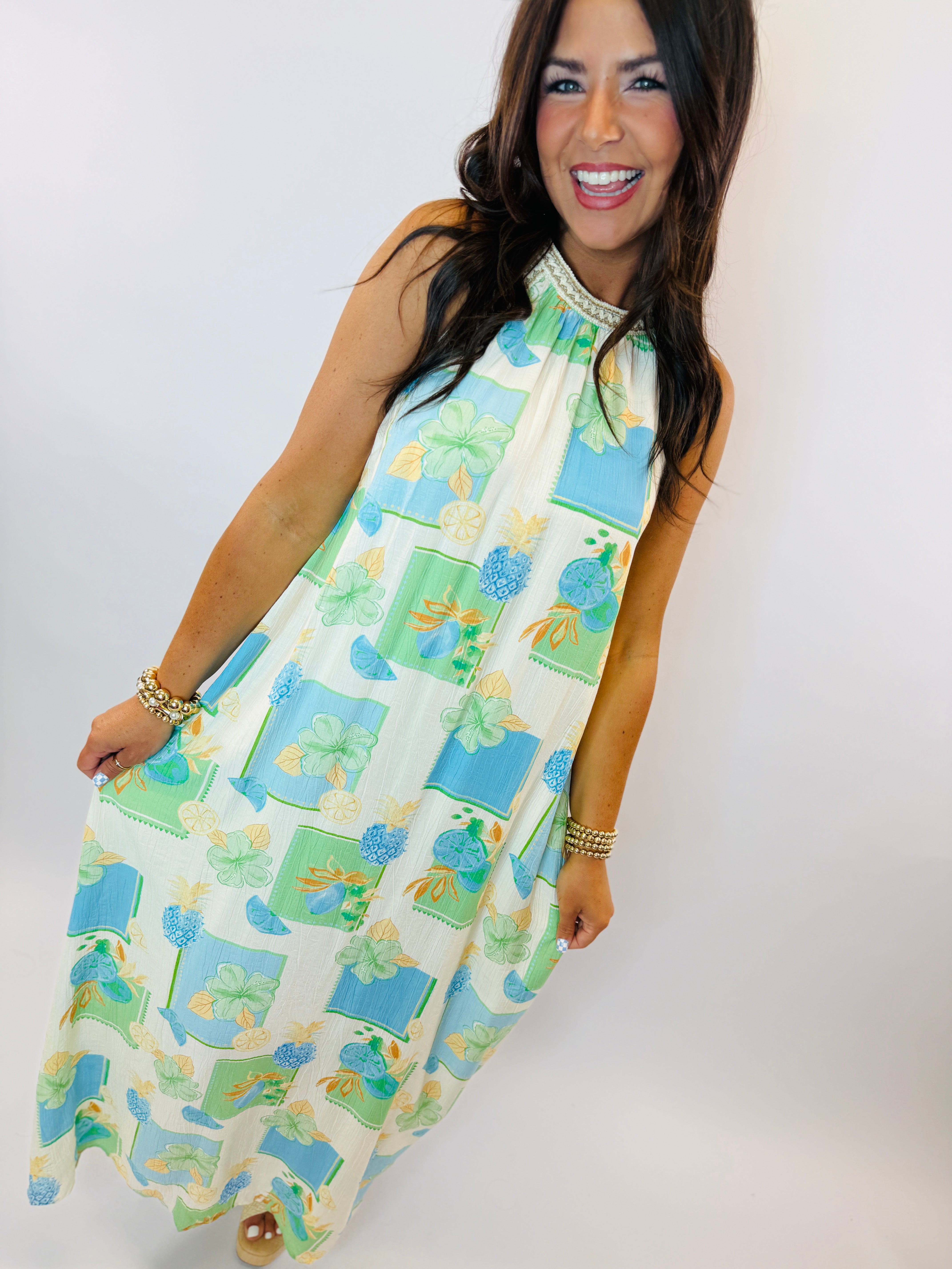 Woman wearing colorful sleeveless Bermuda dress with blue and green floral pattern and beaded neckline.