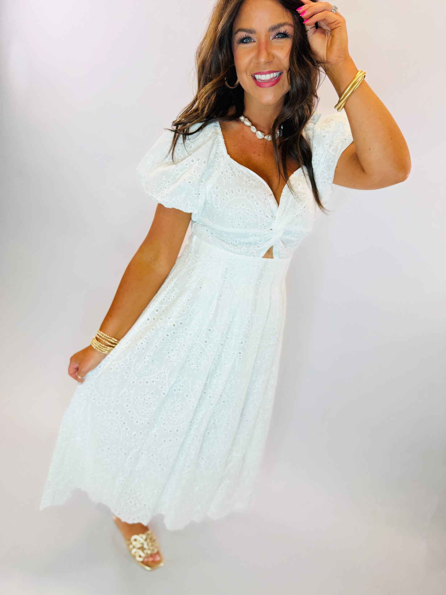 Woman wearing white eyelet midi dress with puff sleeves, V-neckline, and waist cutout detail.