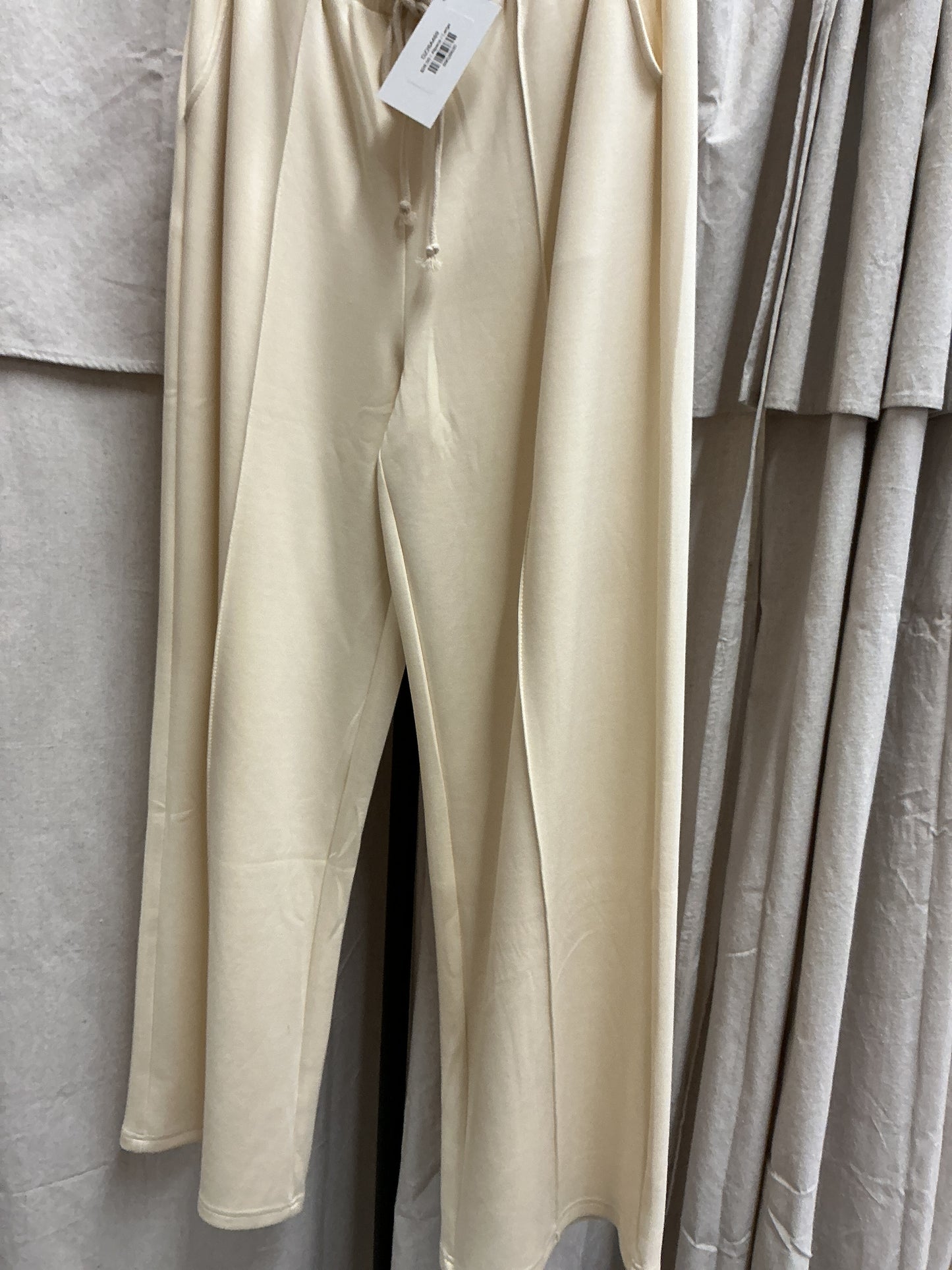 Cream-colored drawstring pants hanging on clothing rack with price tag attached