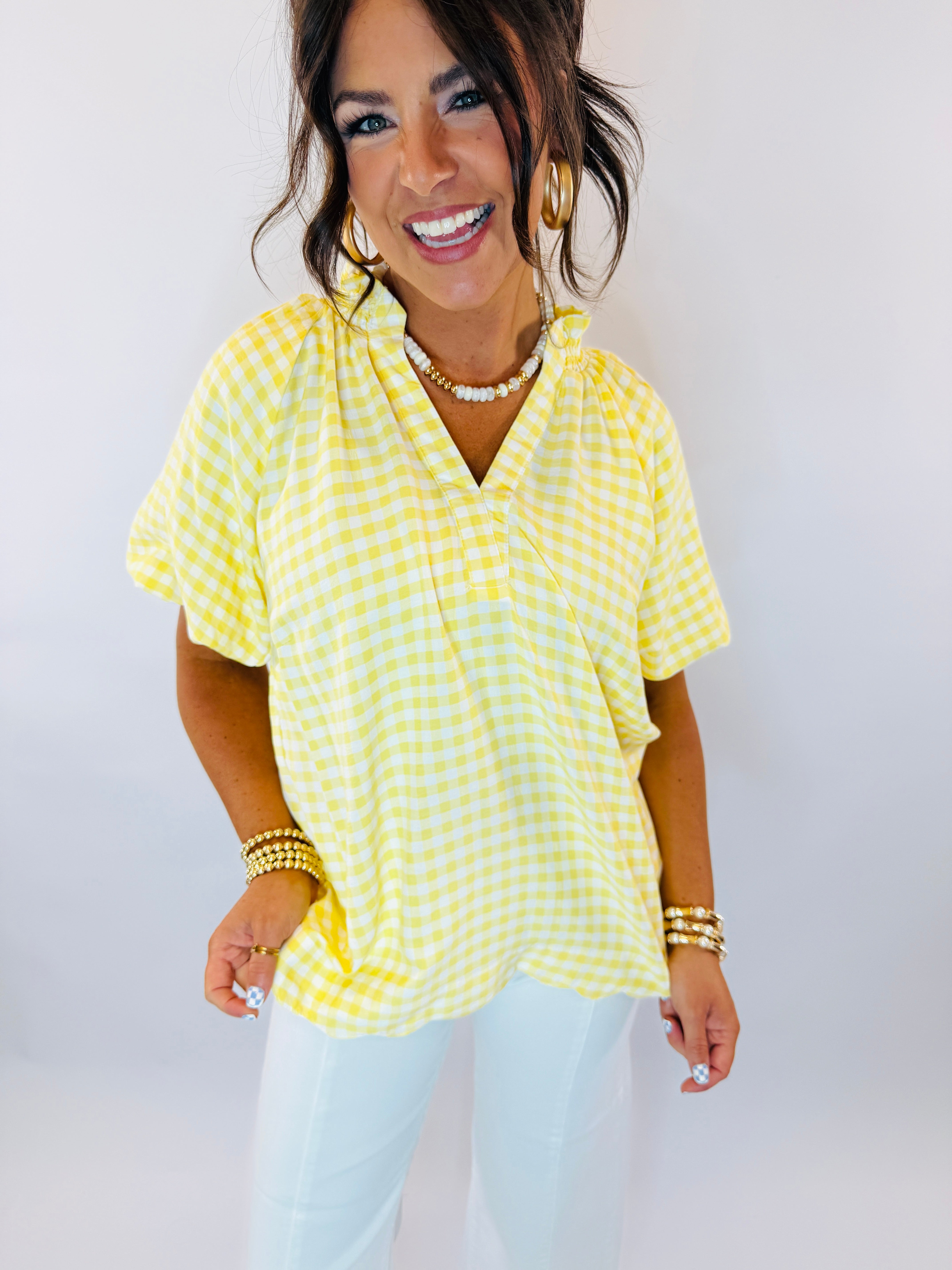 Woman wearing yellow and white gingham checkered short-sleeve top with V-neckline and gold jewelry