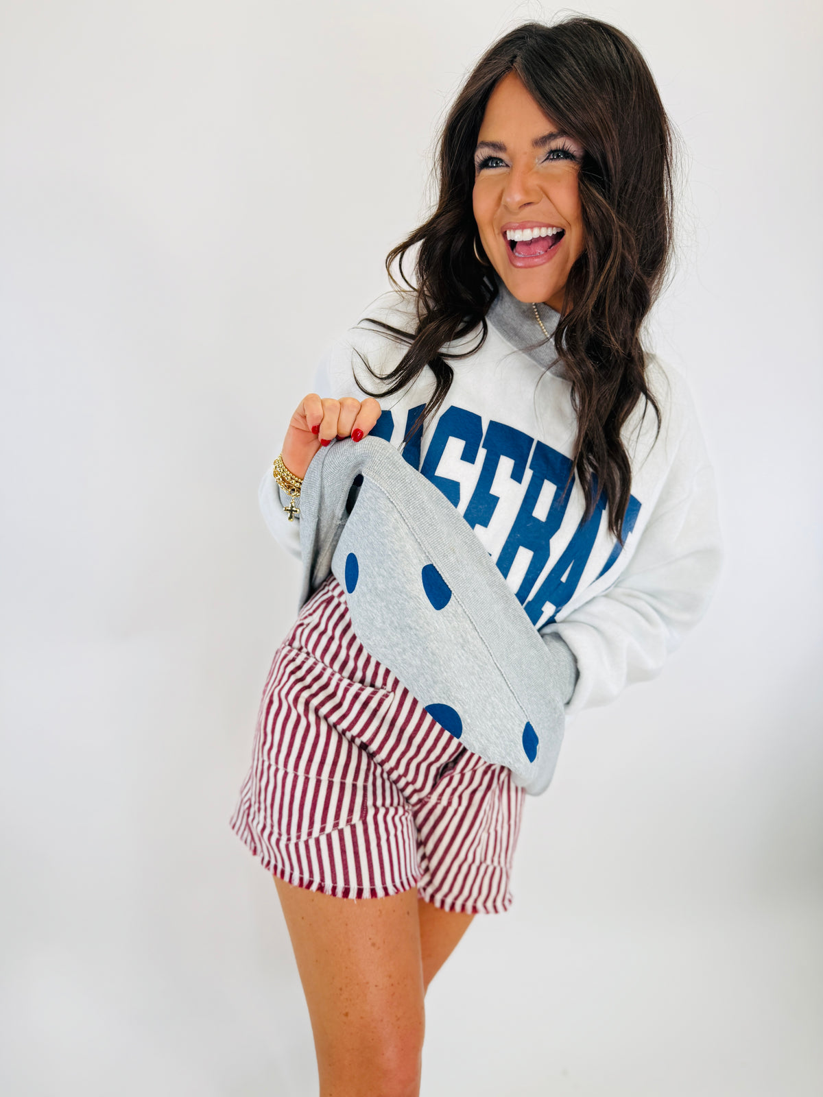 Woman wearing white "VICTORY" sweatshirt and red striped shorts, holding gray polka dot clutch bag