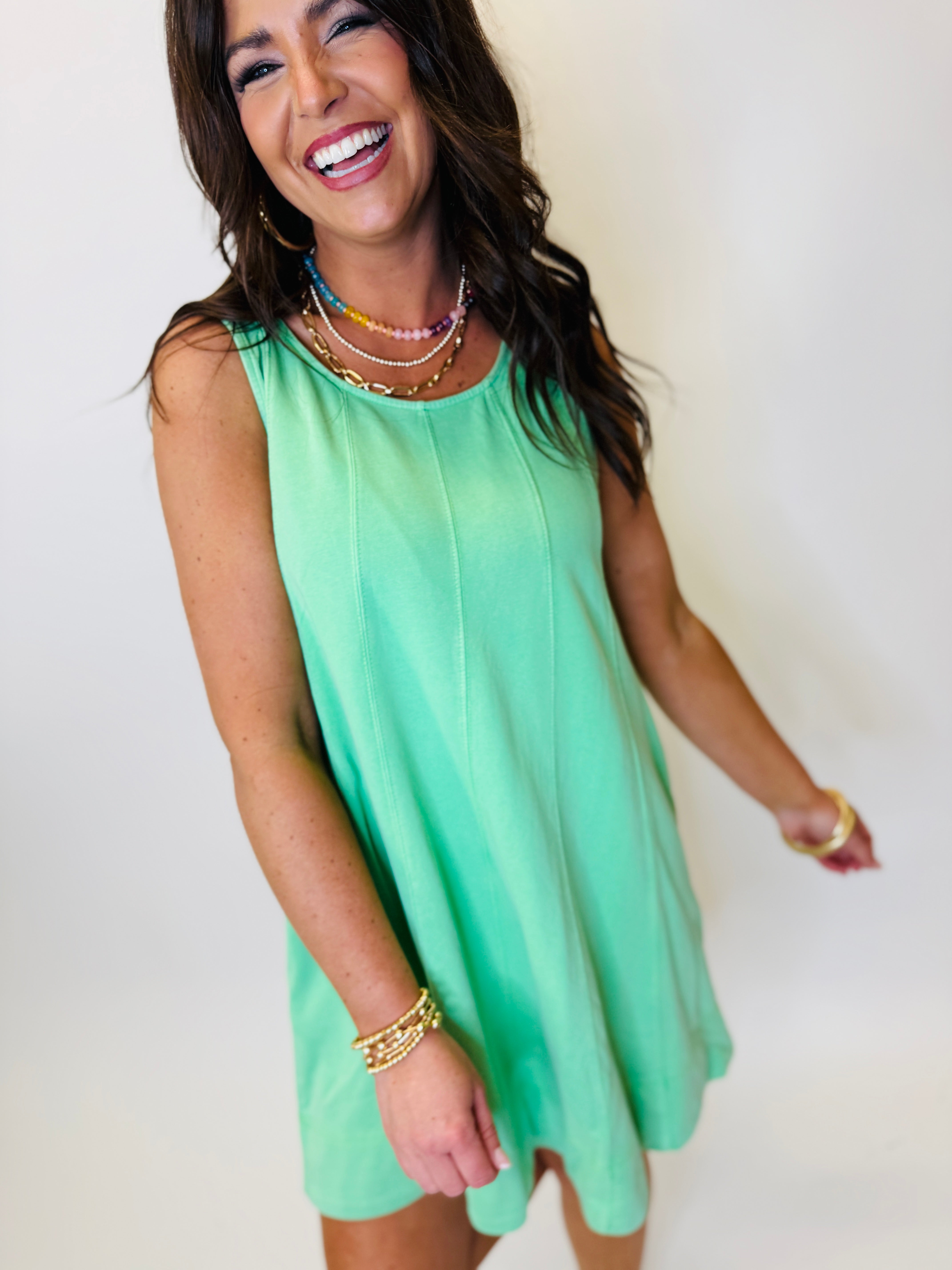 Woman wearing mint green sleeveless swing dress with layered necklaces, smiling against white background.
