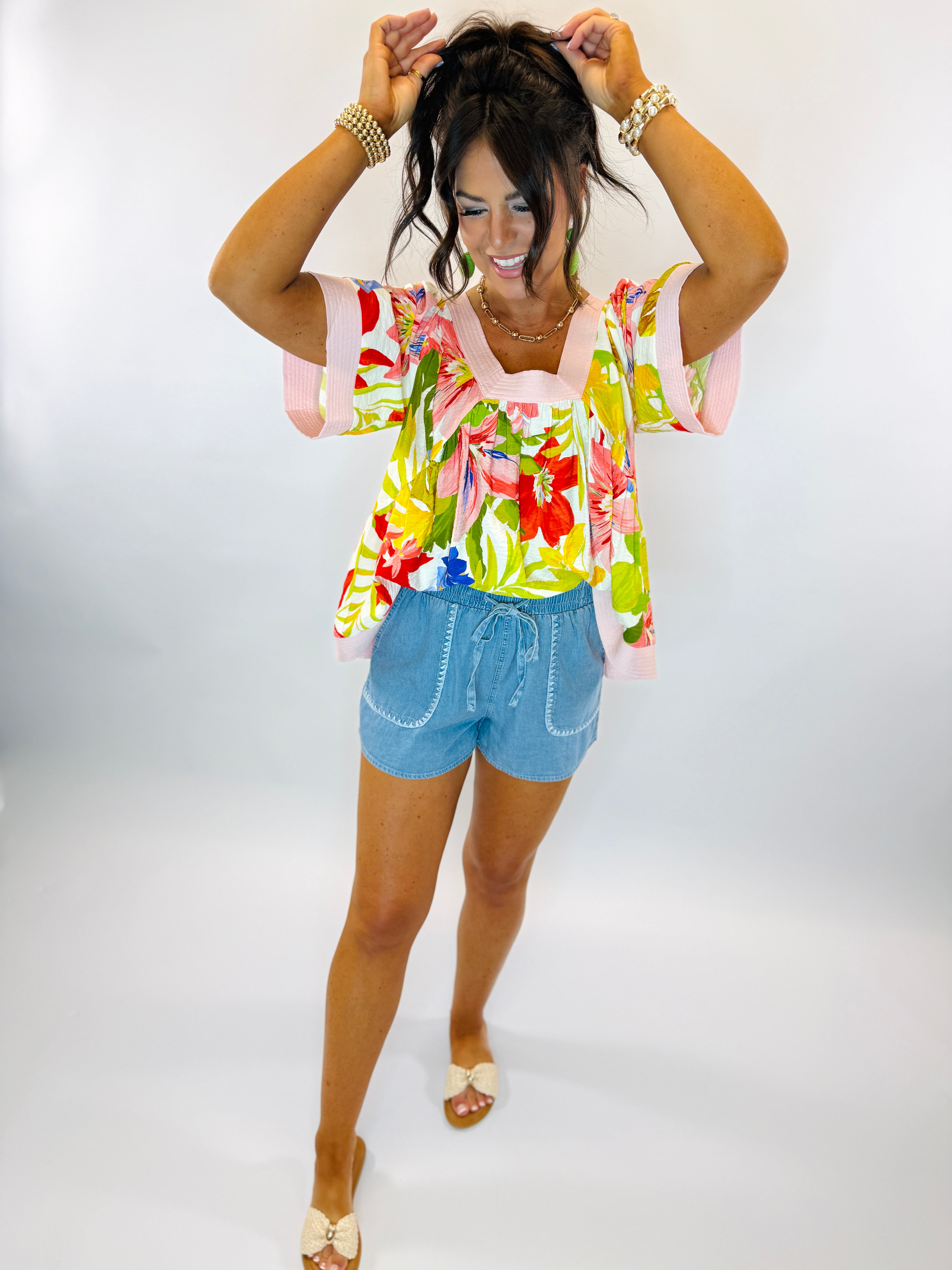 Woman wearing colorful floral Chloe top with puffy sleeves paired with denim shorts and sandals.