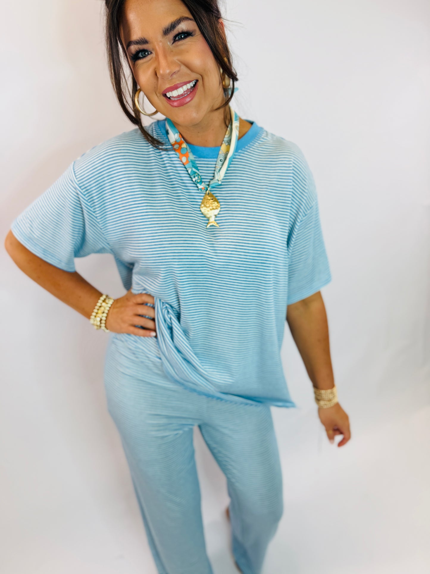 Woman wearing light blue striped ribbed top and matching pants with colorful necklace and gold bracelets
