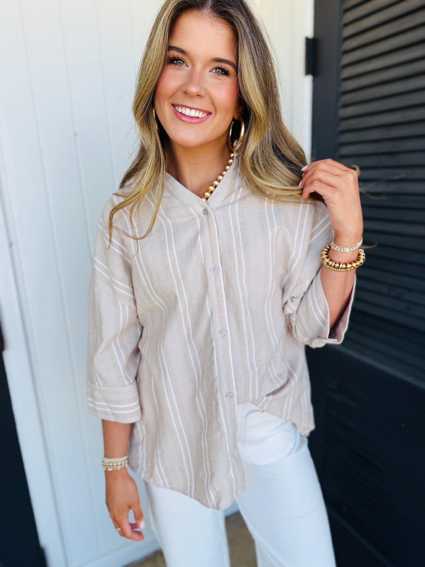 Woman wearing beige striped button-up soft top with pearl jewelry and gold bracelets
