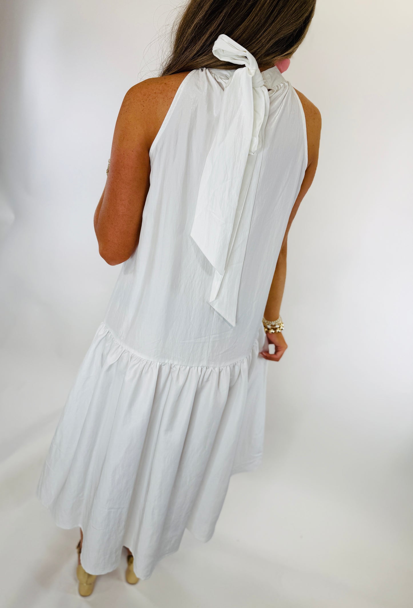 White sleeveless halter dress with neck tie and ruffled hem, shown from back view