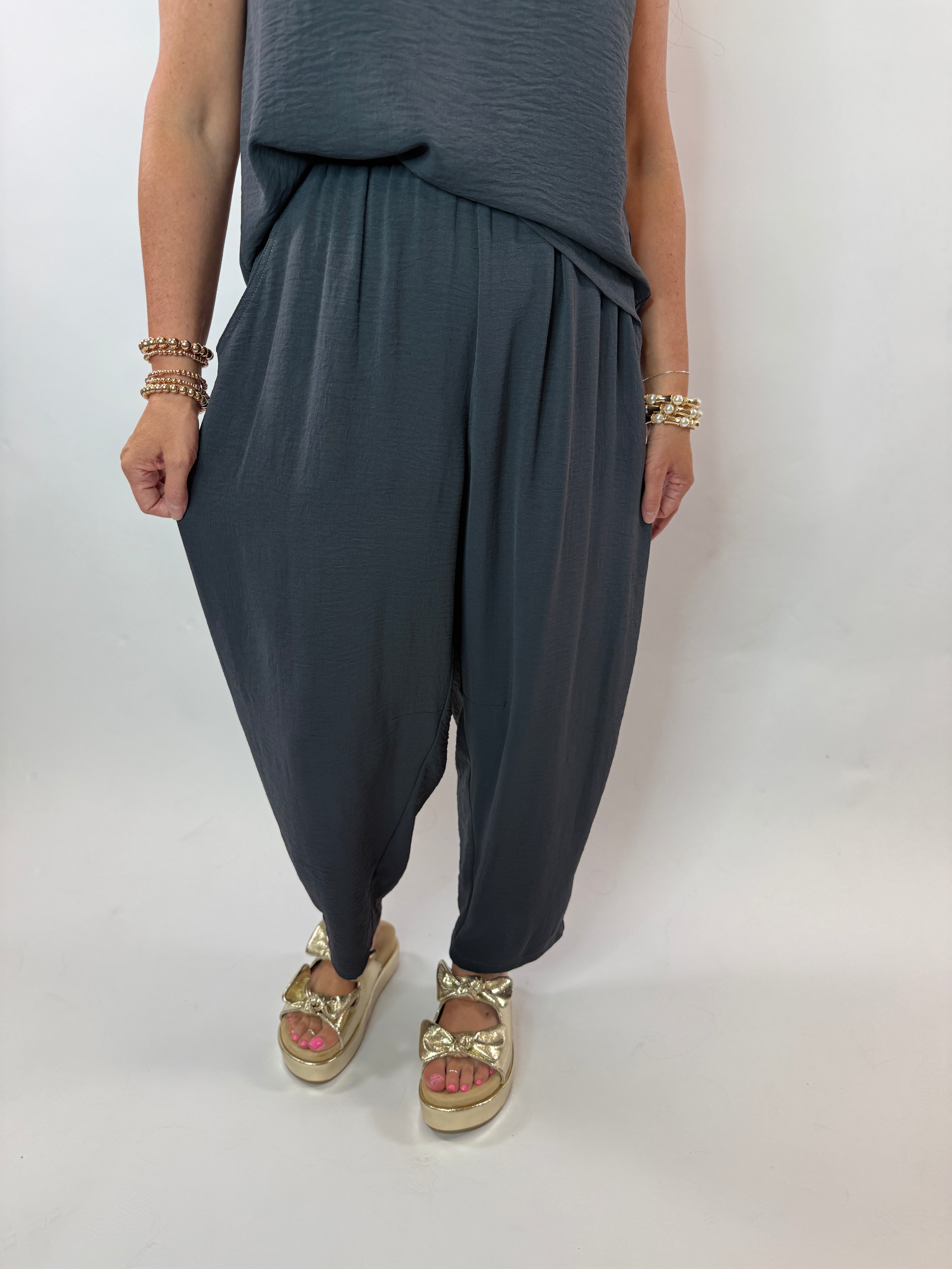 Woman wearing slate blue matching tank top and harem pants set with gold platform sandals and layered bracelets.