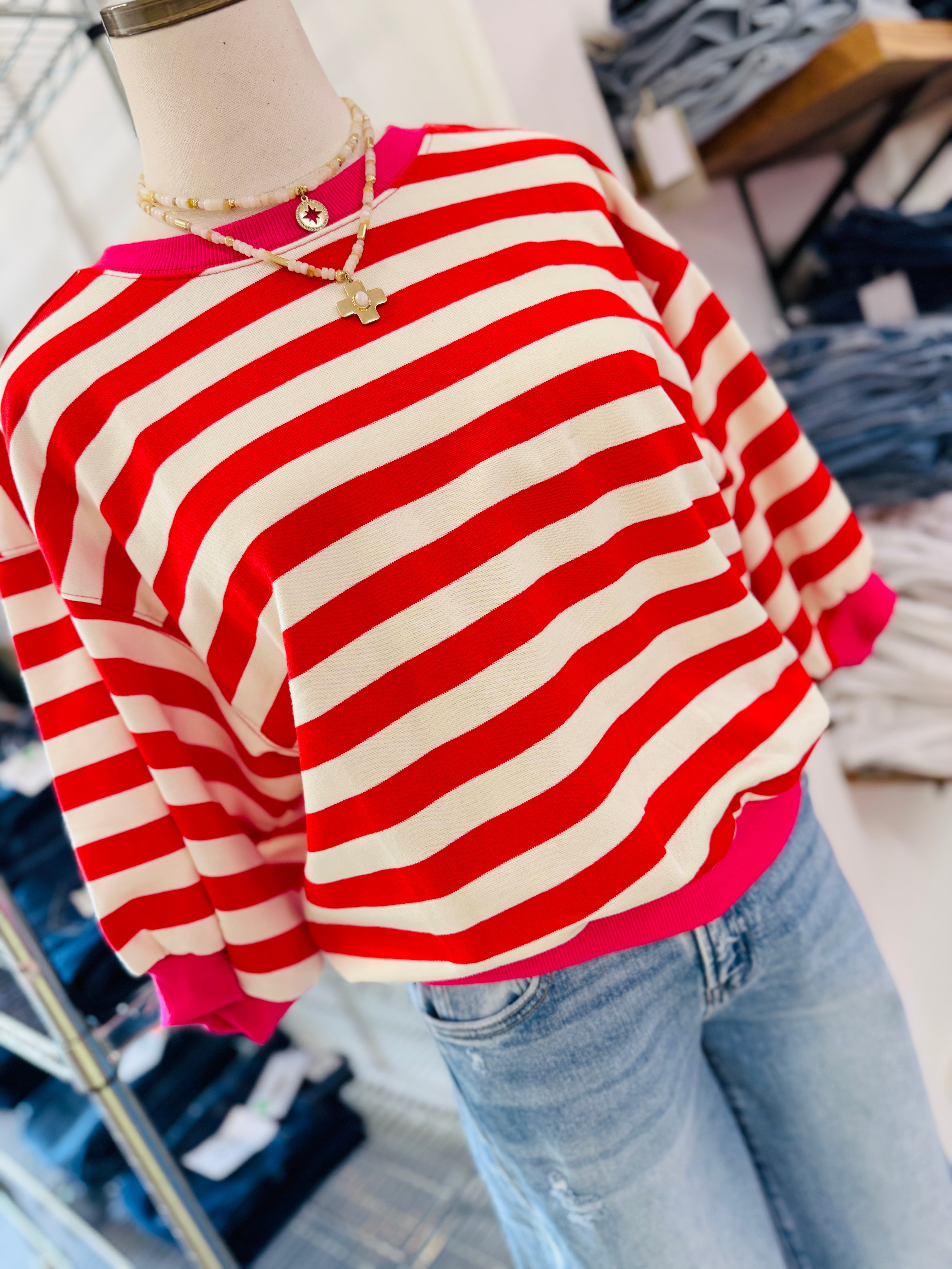 Red and white striped sweater with pink trim displayed on mannequin, paired with blue jeans.
