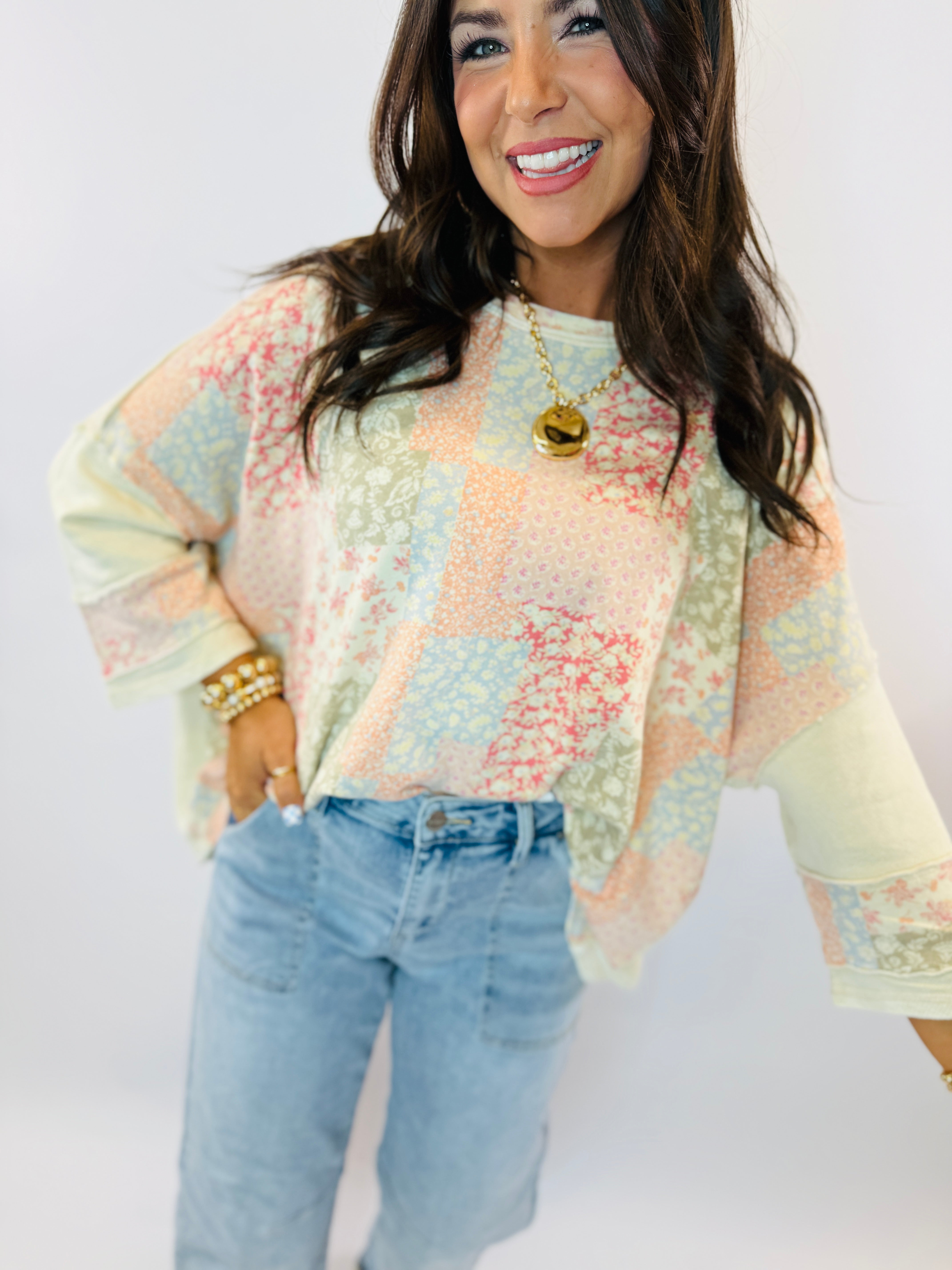 Woman wearing colorful pastel patchwork long-sleeve top with balloon sleeves, paired with light blue jeans and gold jewelry.