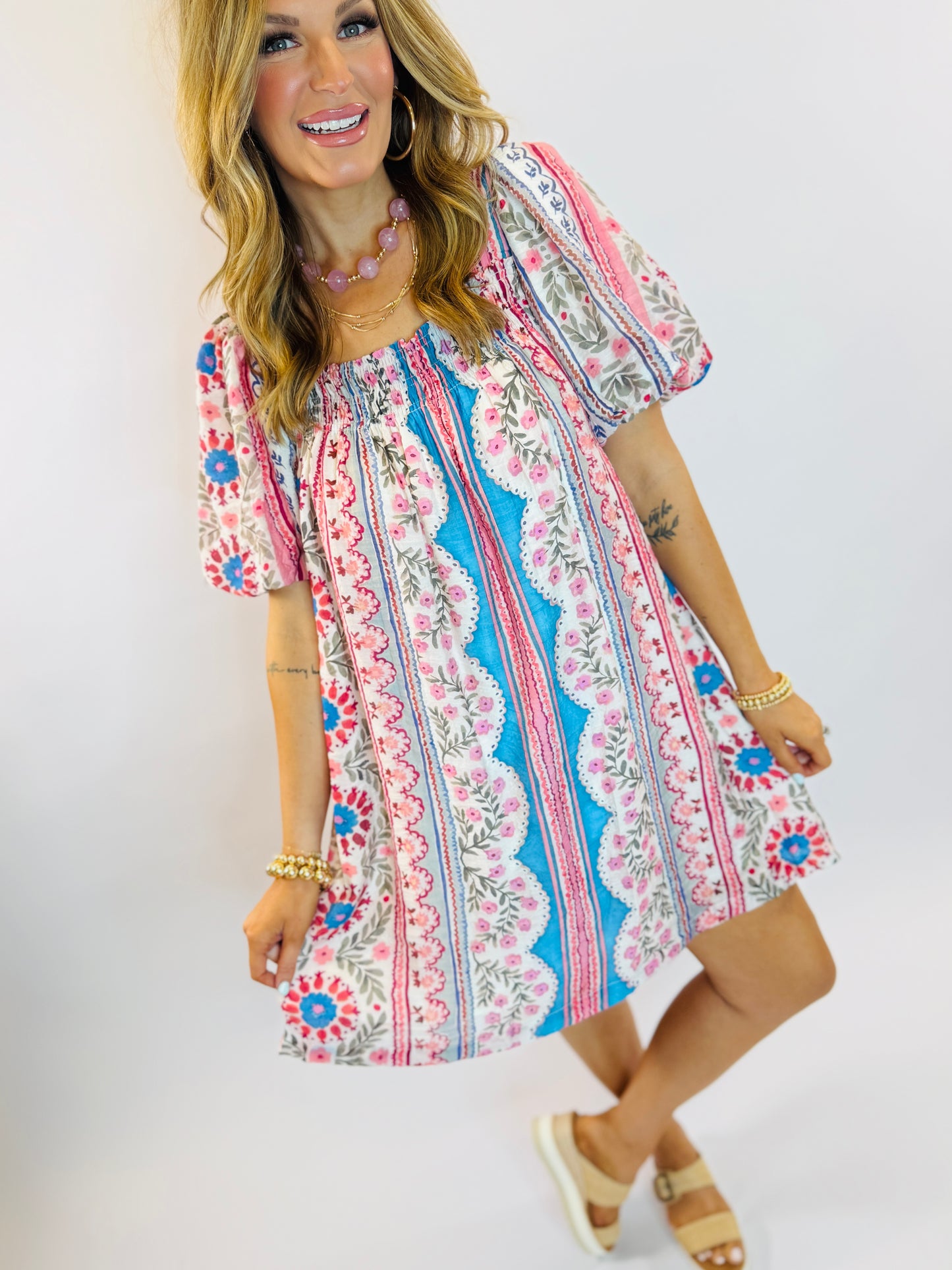 Woman wearing colorful floral patterned short-sleeve dress with off-shoulder neckline and bohemian print design.