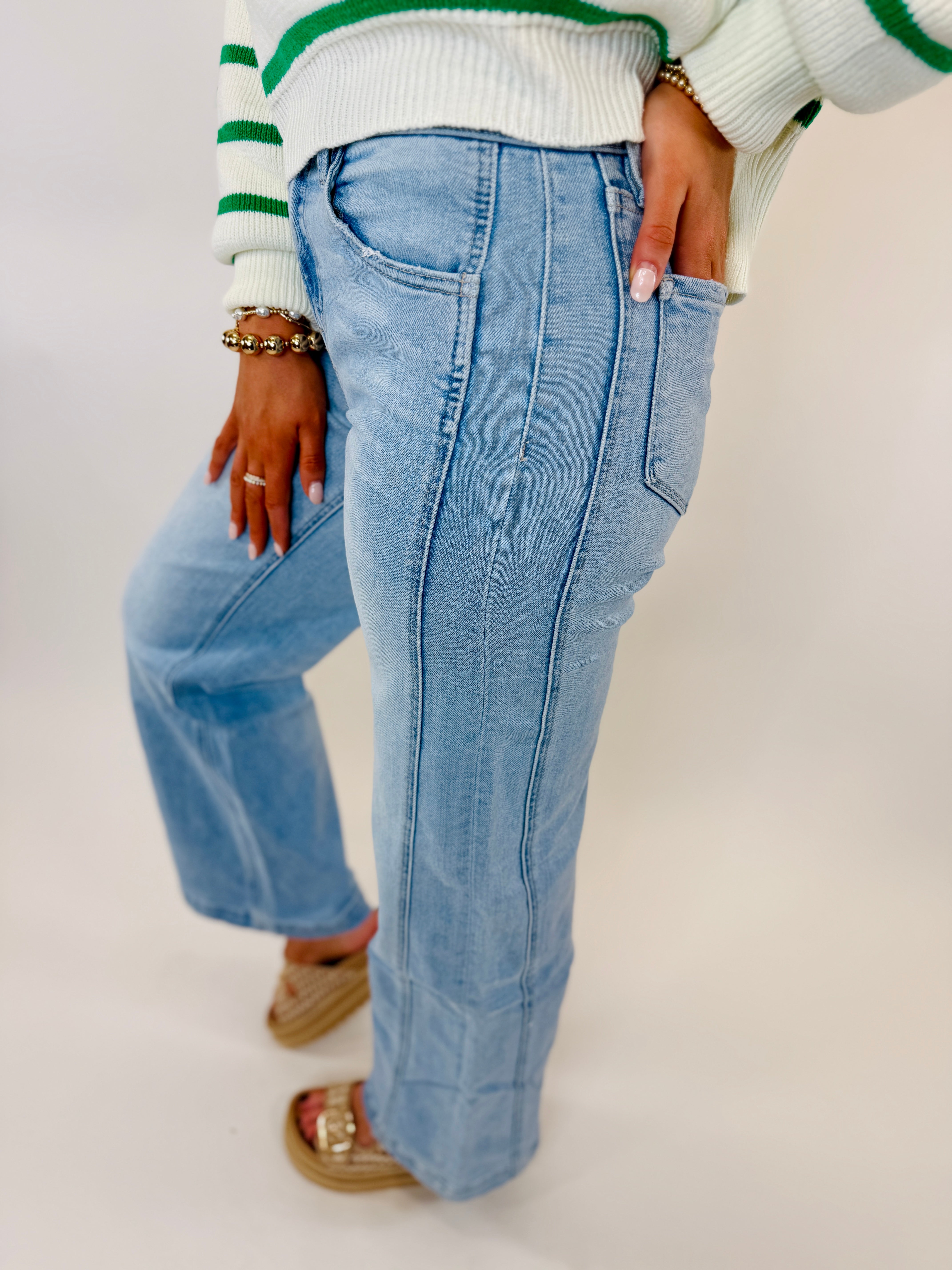 Light blue structured denim jeans with seam detailing, worn with white striped sweater and platform sandals.