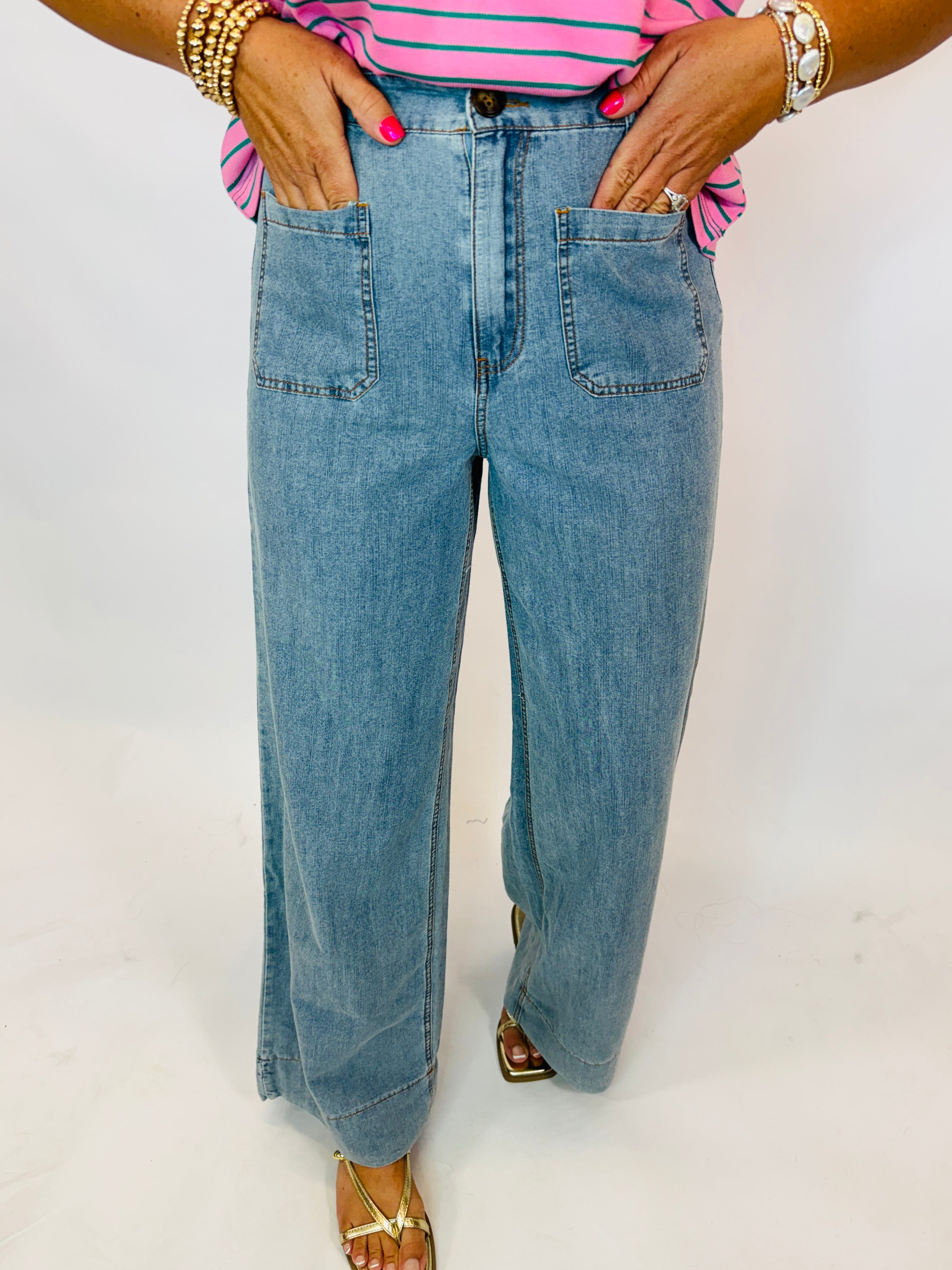 Light wash wide-leg denim jeans with front patch pockets, worn with pink striped top and gold sandals.