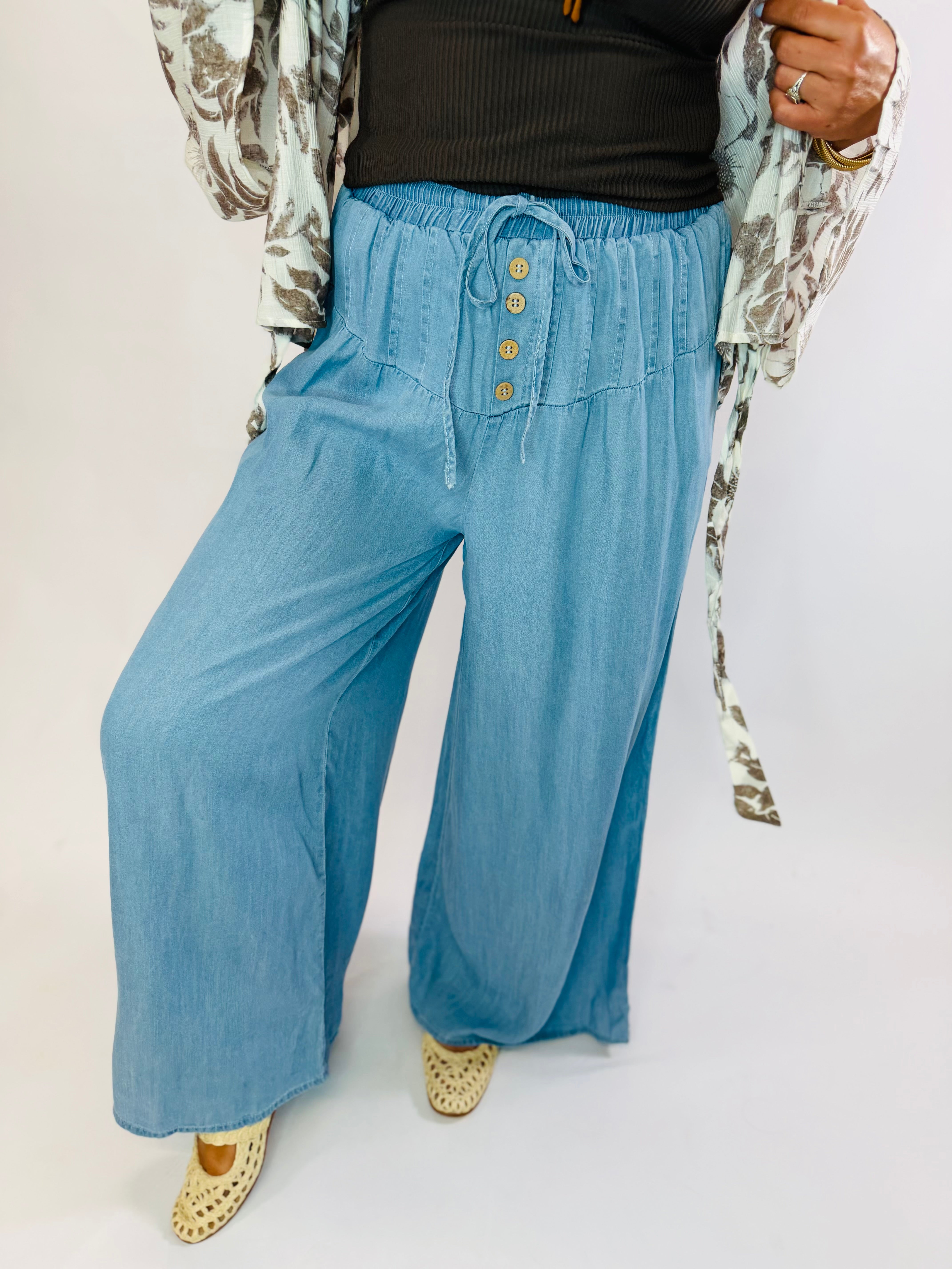 Wide-leg light blue chambray Phoebe Pants with elastic drawstring waist and decorative buttons.