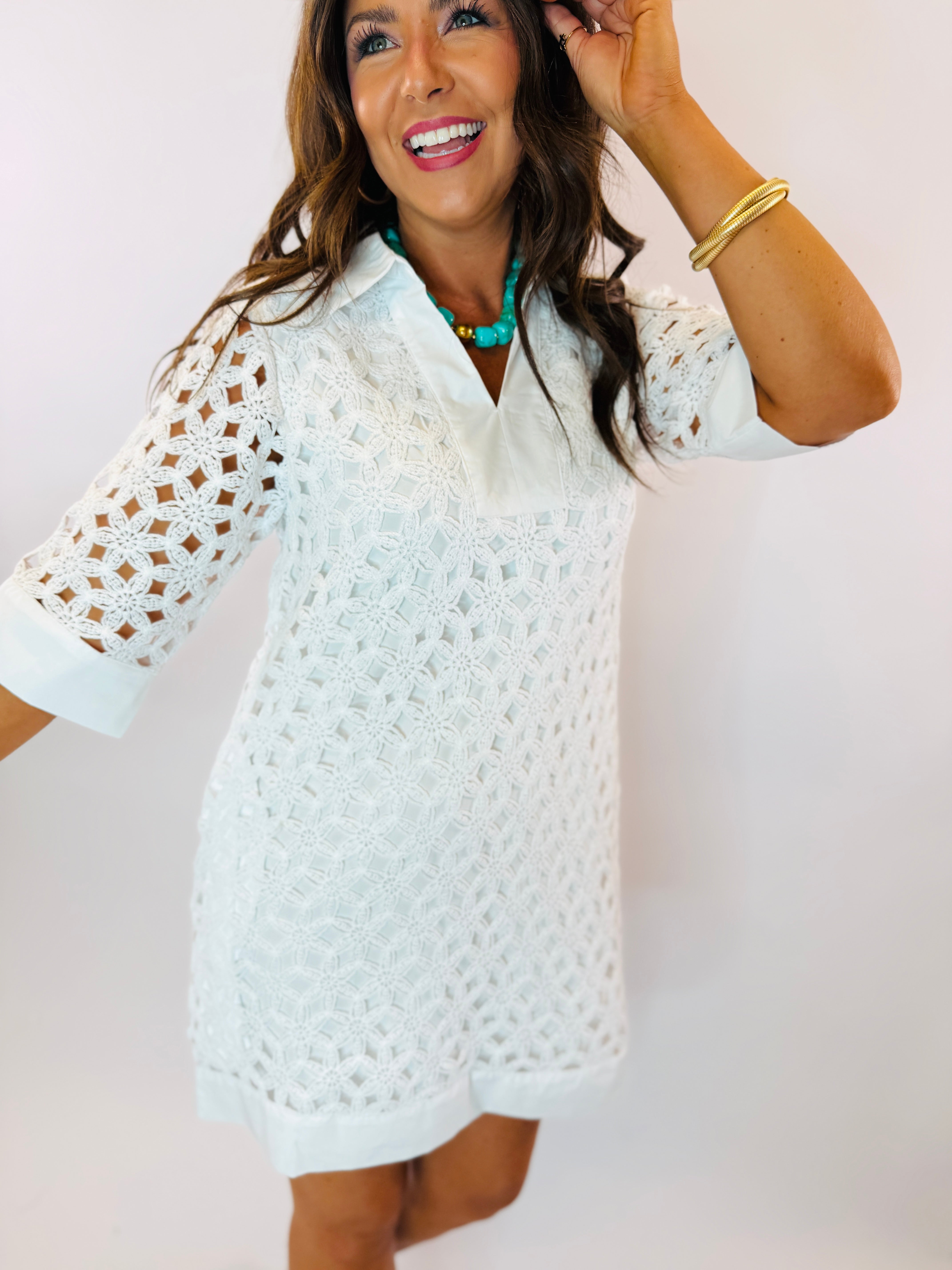 White eyelet lace mini dress with collar neckline and elbow-length sleeves, styled with turquoise necklace.