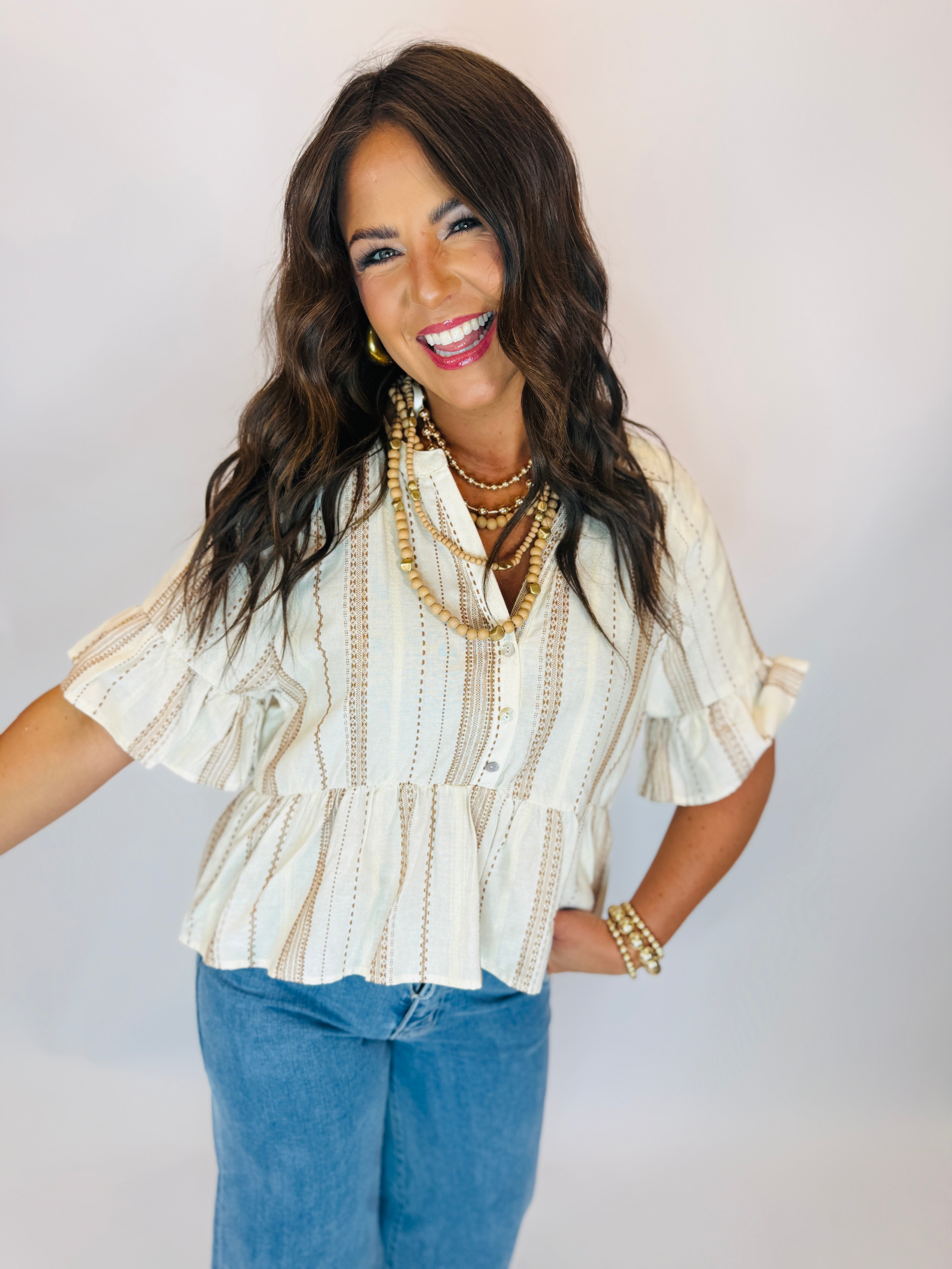 Woman wearing cream and tan striped peplum blouse with ruffle sleeves, paired with blue jeans.