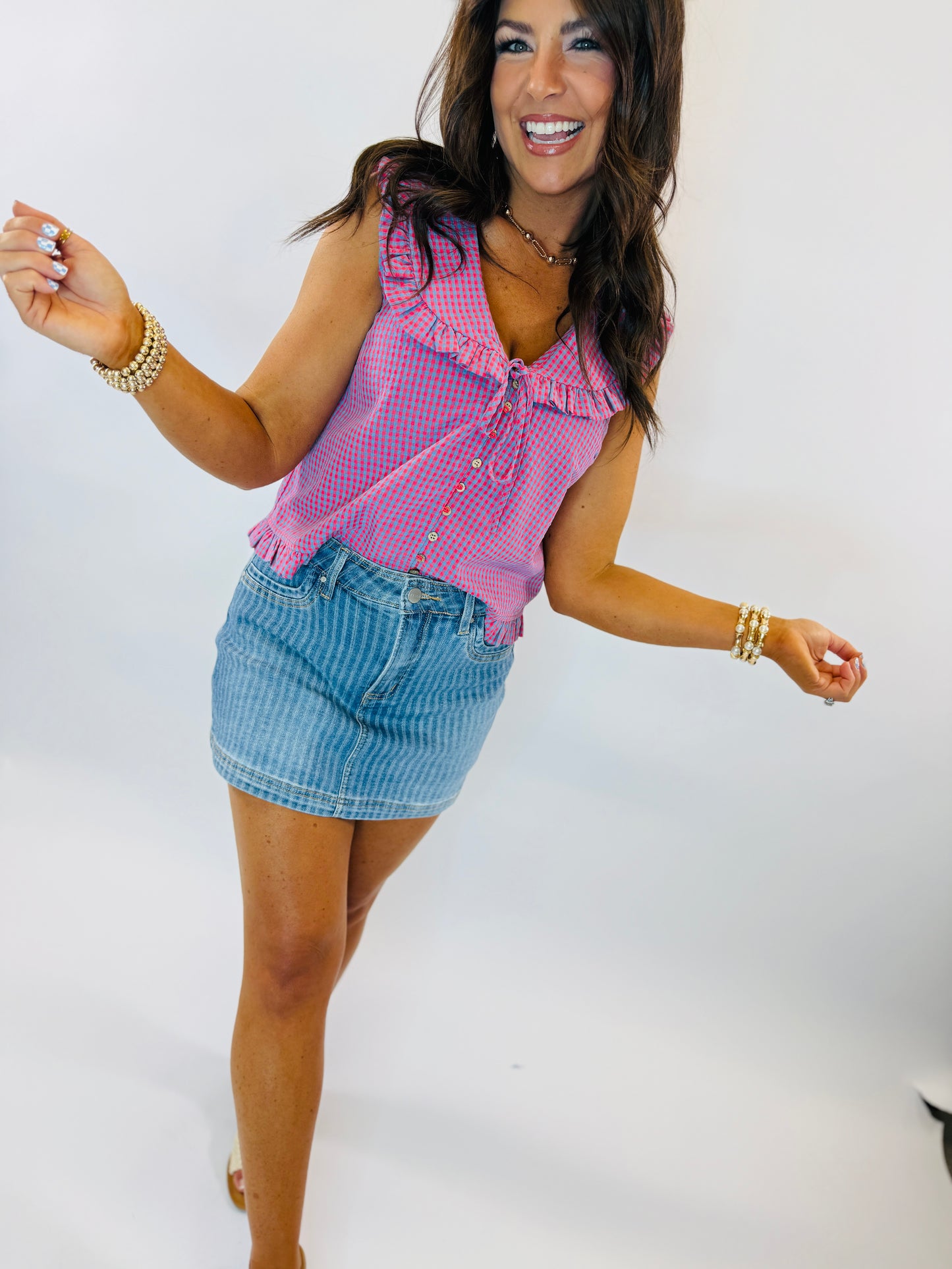 Woman wearing pink gingham sleeveless top and blue striped denim mini skirt, smiling and posing with arms outstretched.
