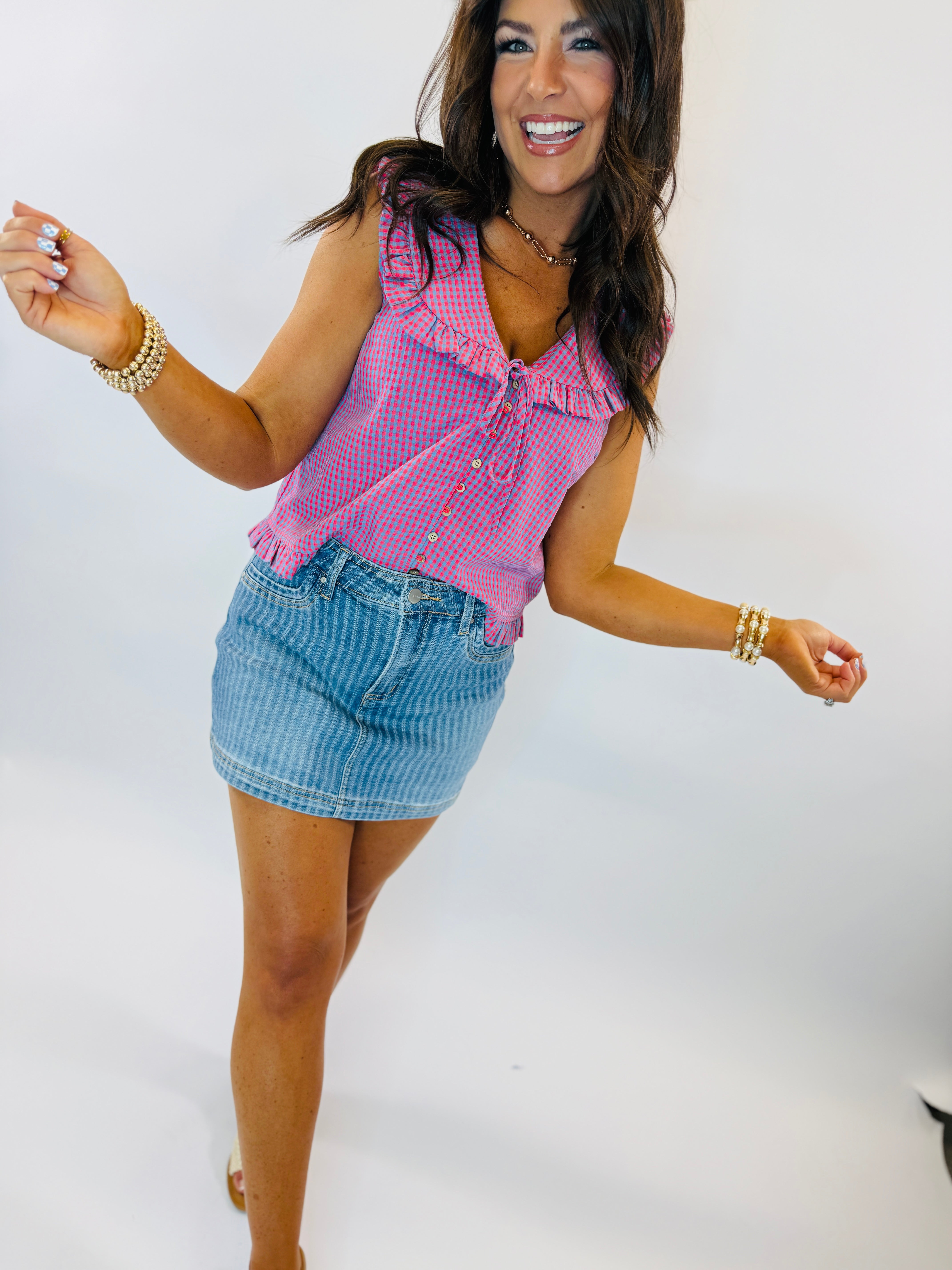 Woman wearing pink gingham sleeveless top and blue striped denim mini skirt, smiling and posing with arms outstretched.