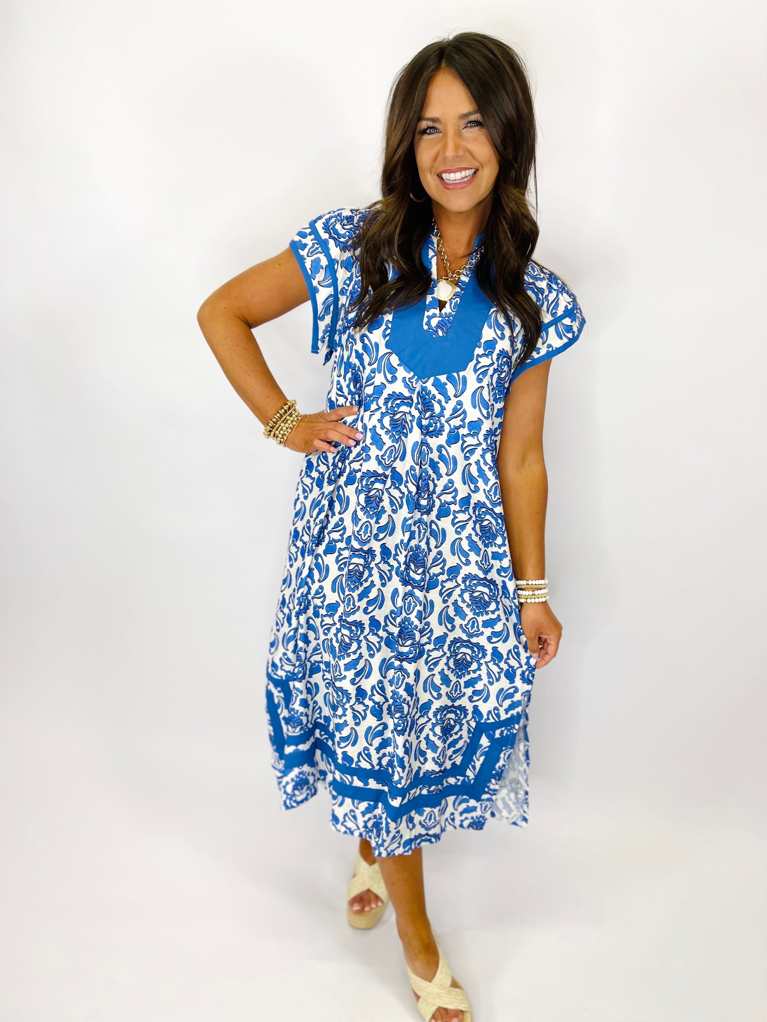 Woman wearing blue and white floral patterned Emery dress with short sleeves and midi length.