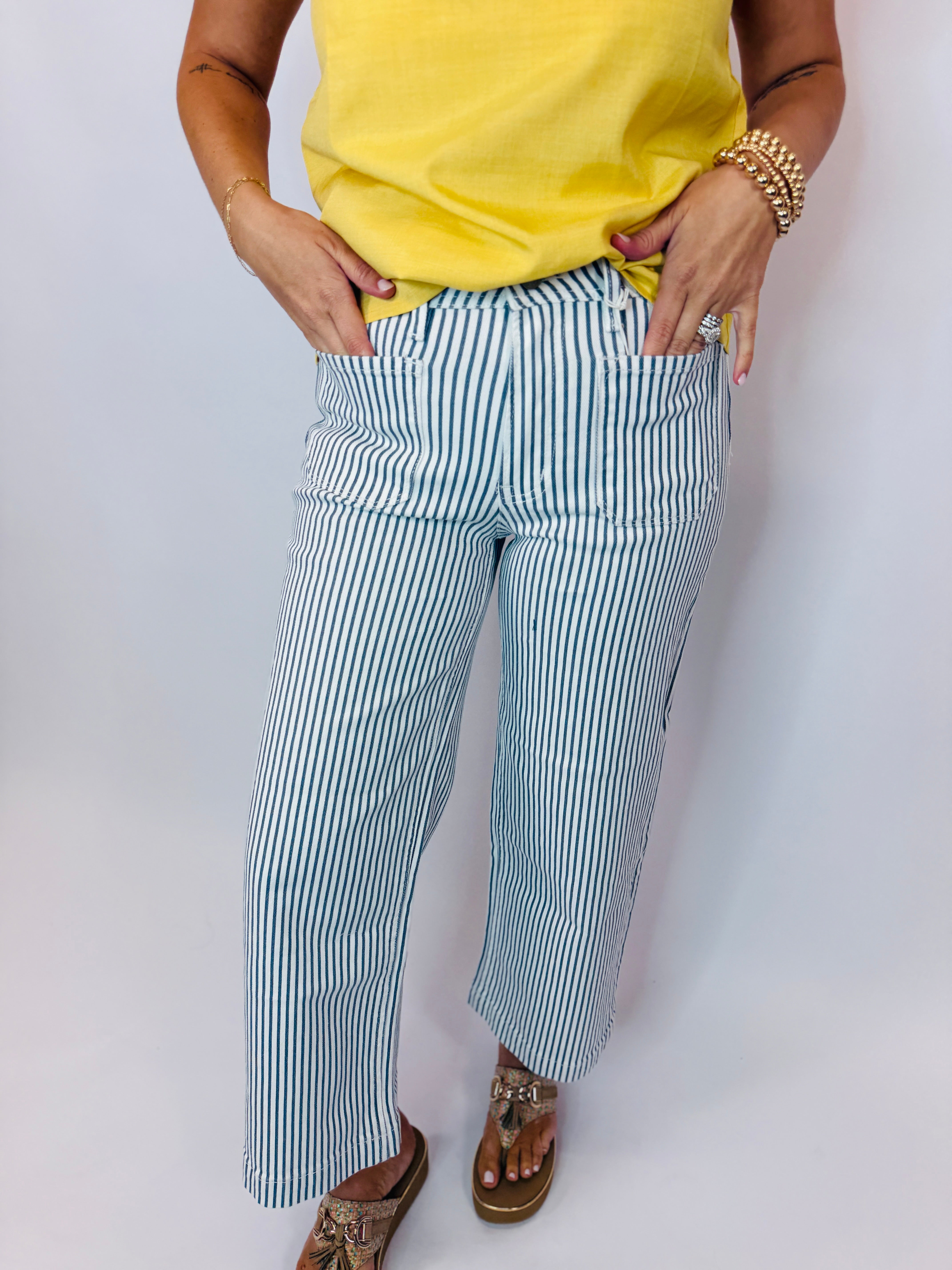 Woman wearing yellow top and blue and white striped wide-leg denim pants with brown sandals.