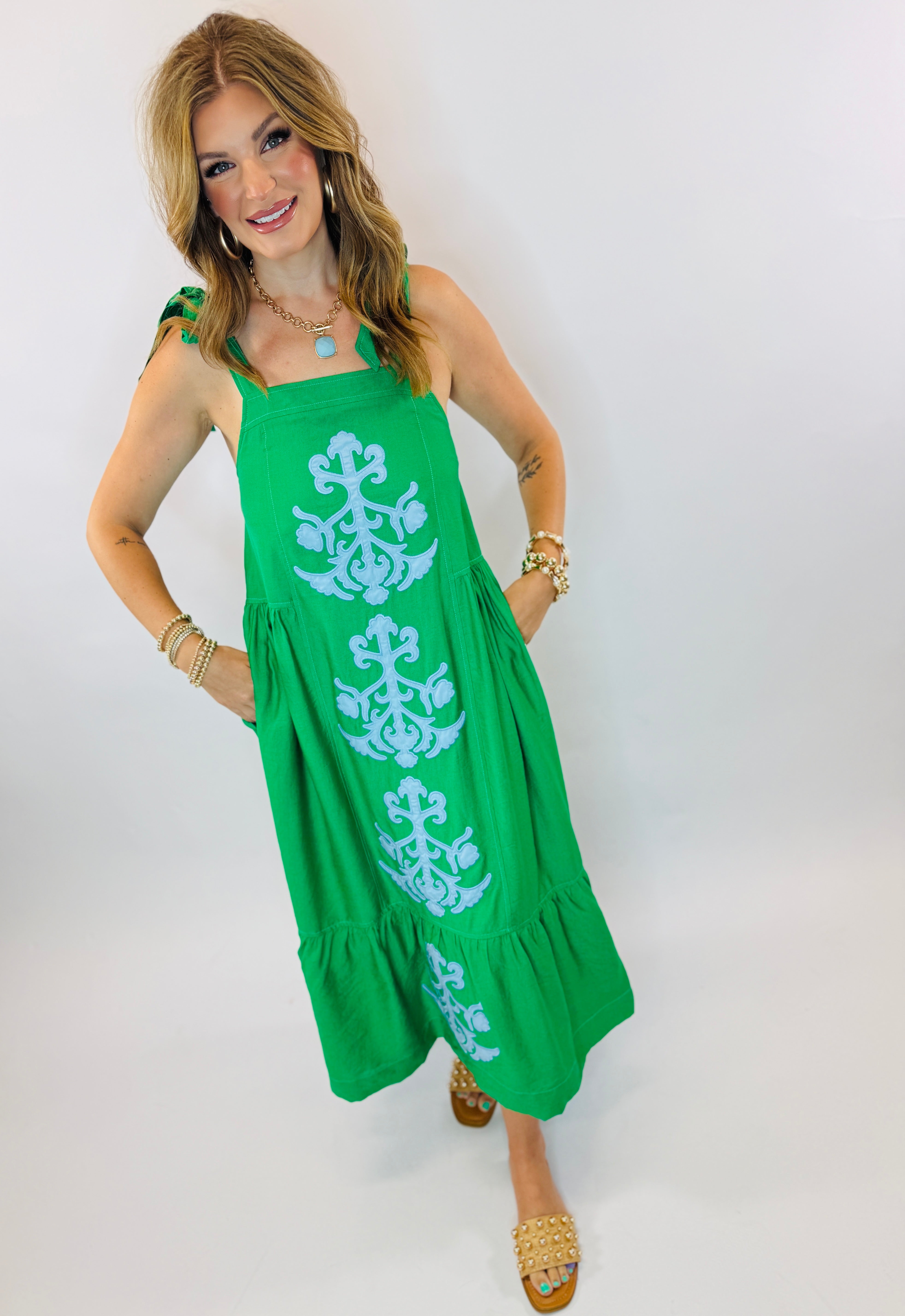 Woman wearing bright green midi dress with white embroidered floral pattern and tiered ruffle hem