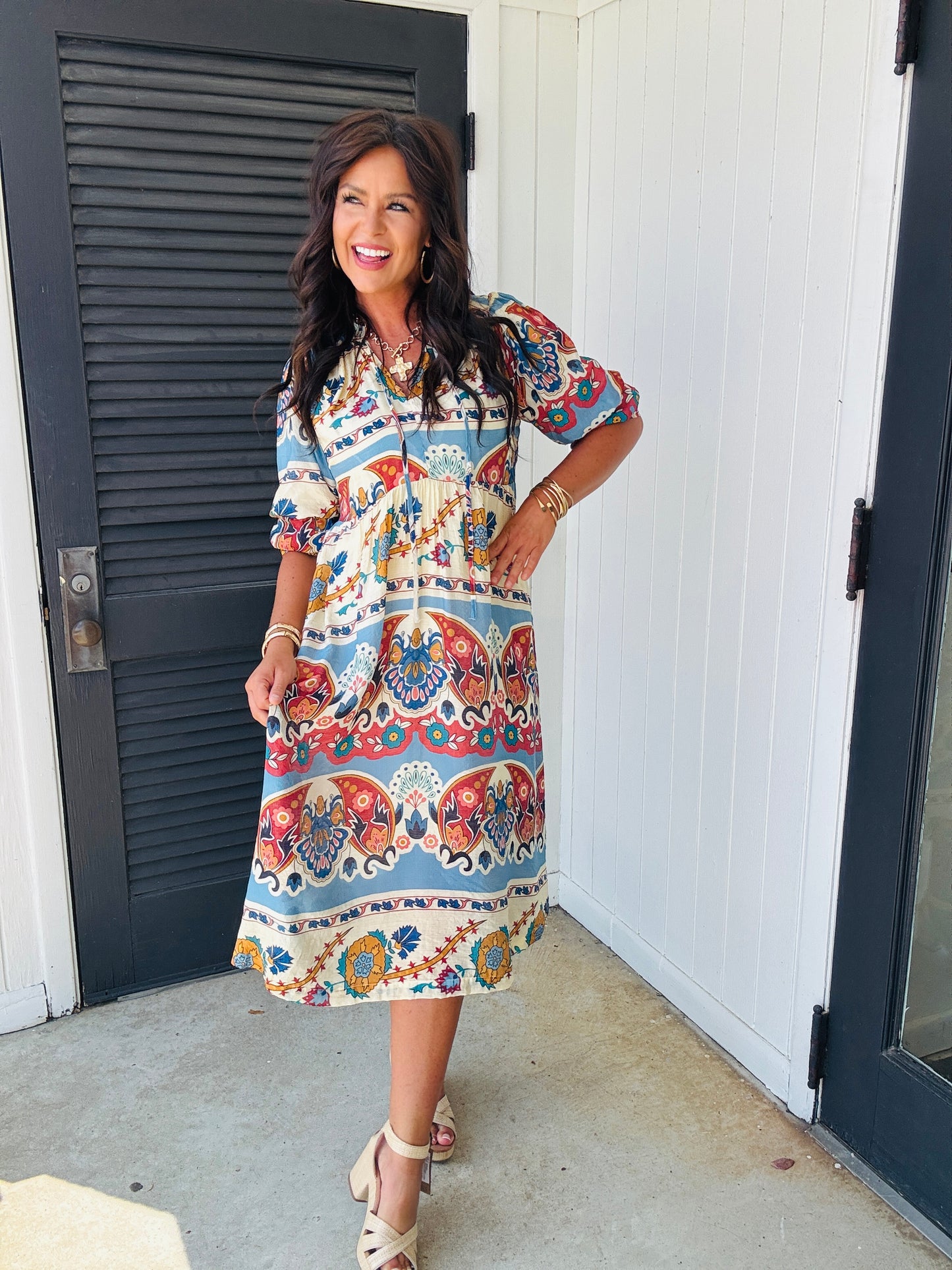 Woman wearing colorful patterned Kara midi dress with paisley and floral print, standing on concrete patio.
