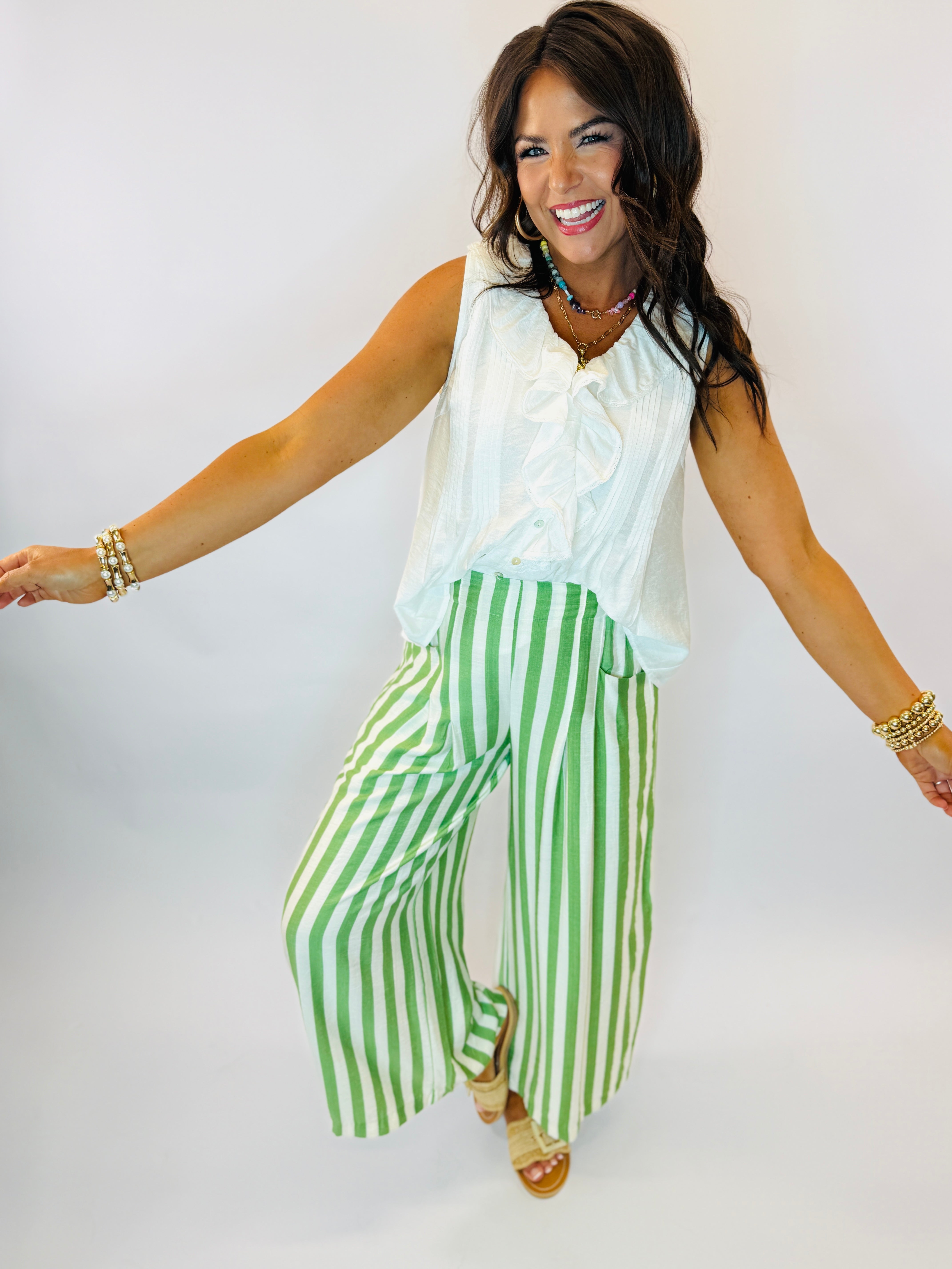 Woman wearing white sleeveless top and green and white striped wide-leg pants with gold accessories
