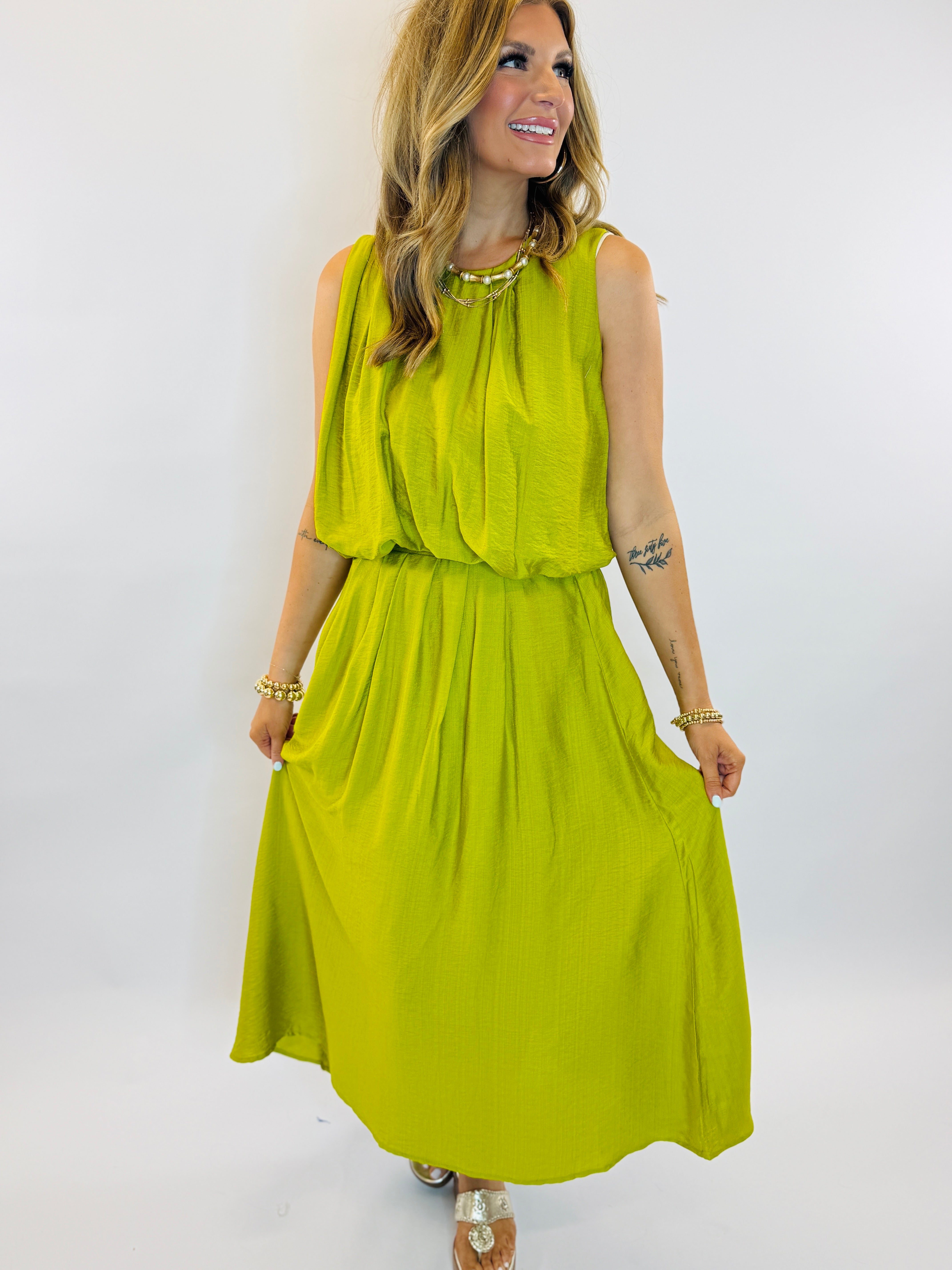 Woman wearing bright green sleeveless maxi dress with gathered waist and flowing skirt, styled with gold jewelry.
