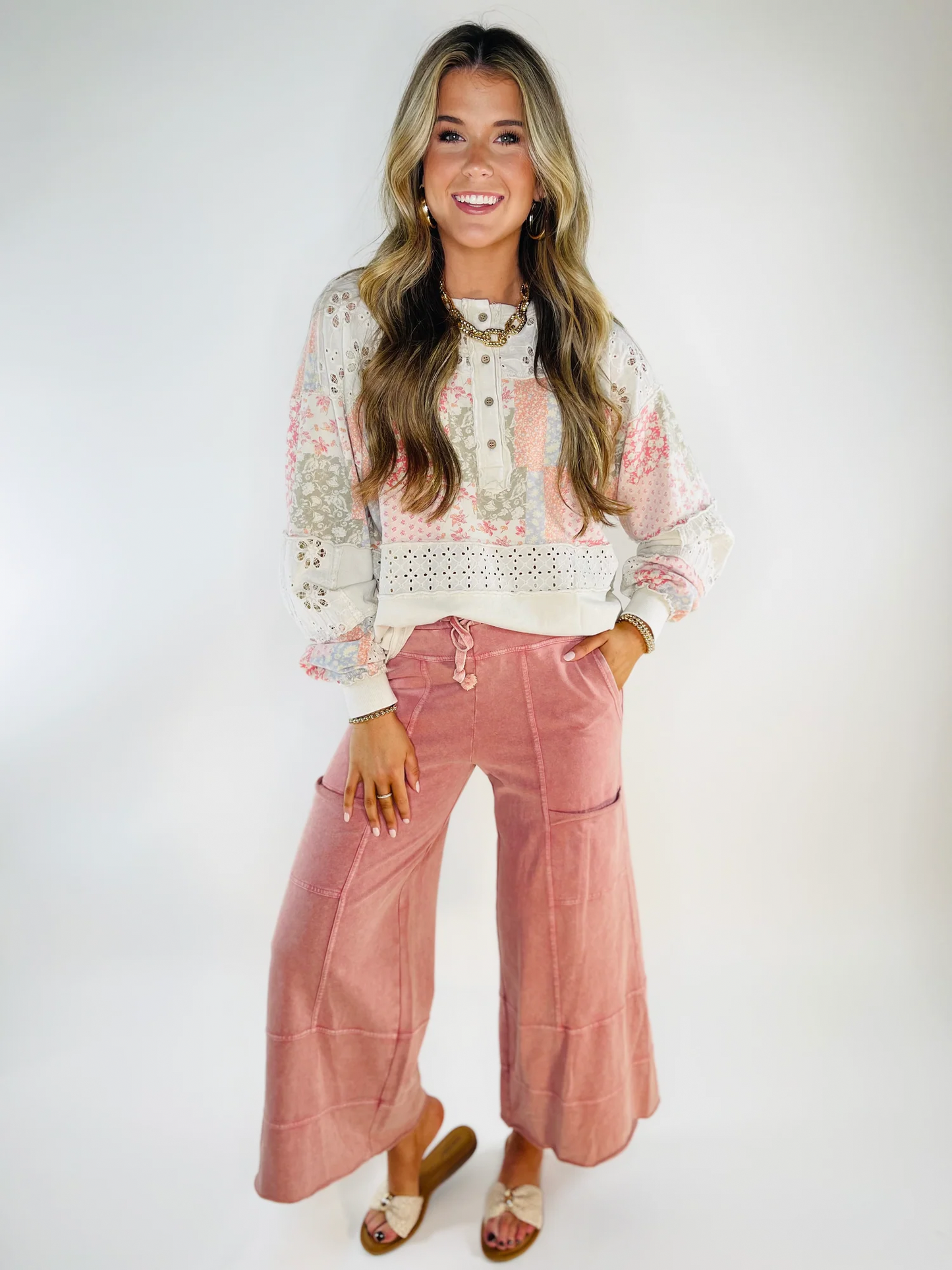 Woman wearing floral patchwork Finley Everyday Top with eyelet trim and button details, paired with pink wide-leg pants