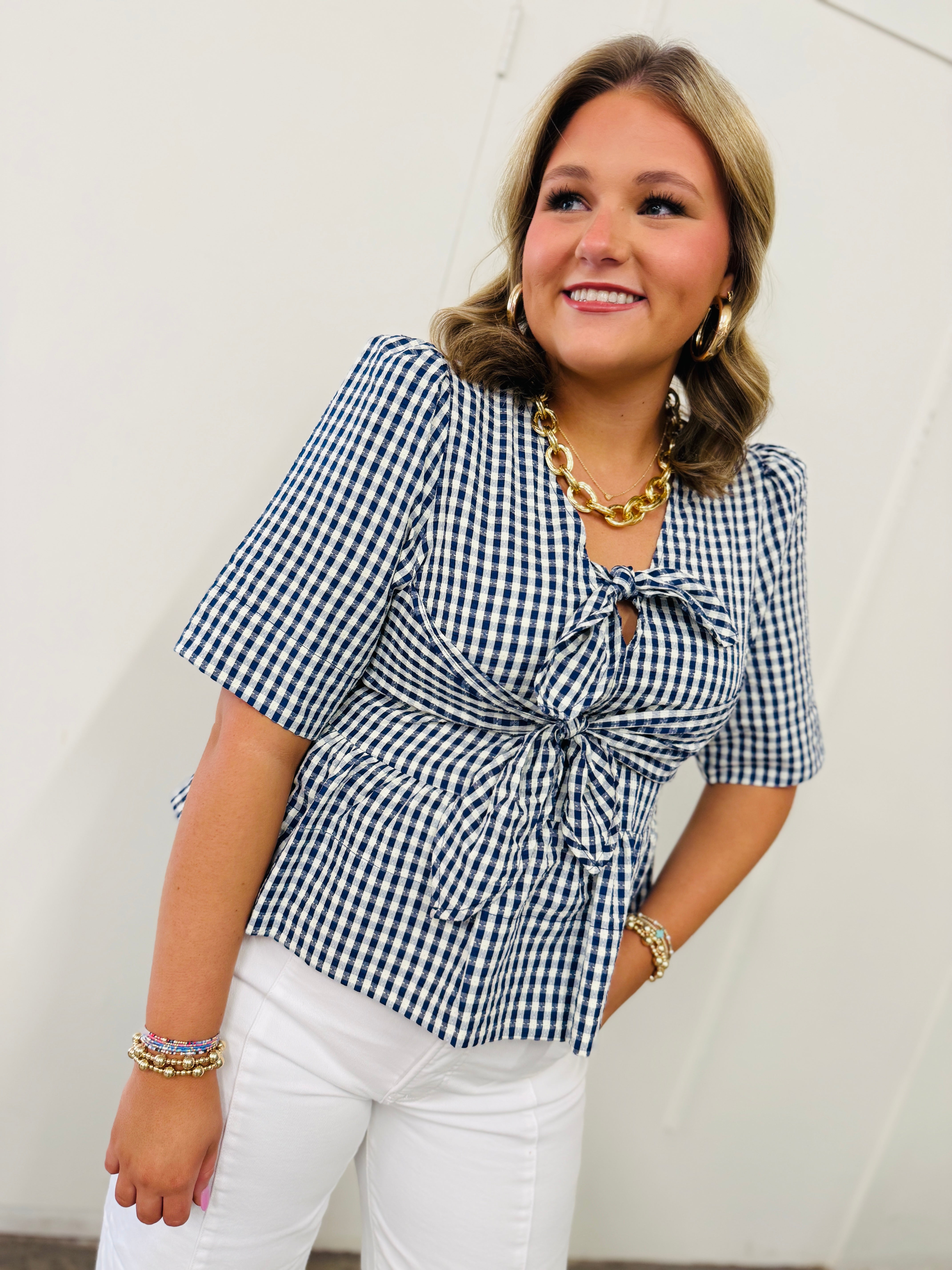 Woman wearing blue and white gingham checked short-sleeve top with tie-front detail and white pants