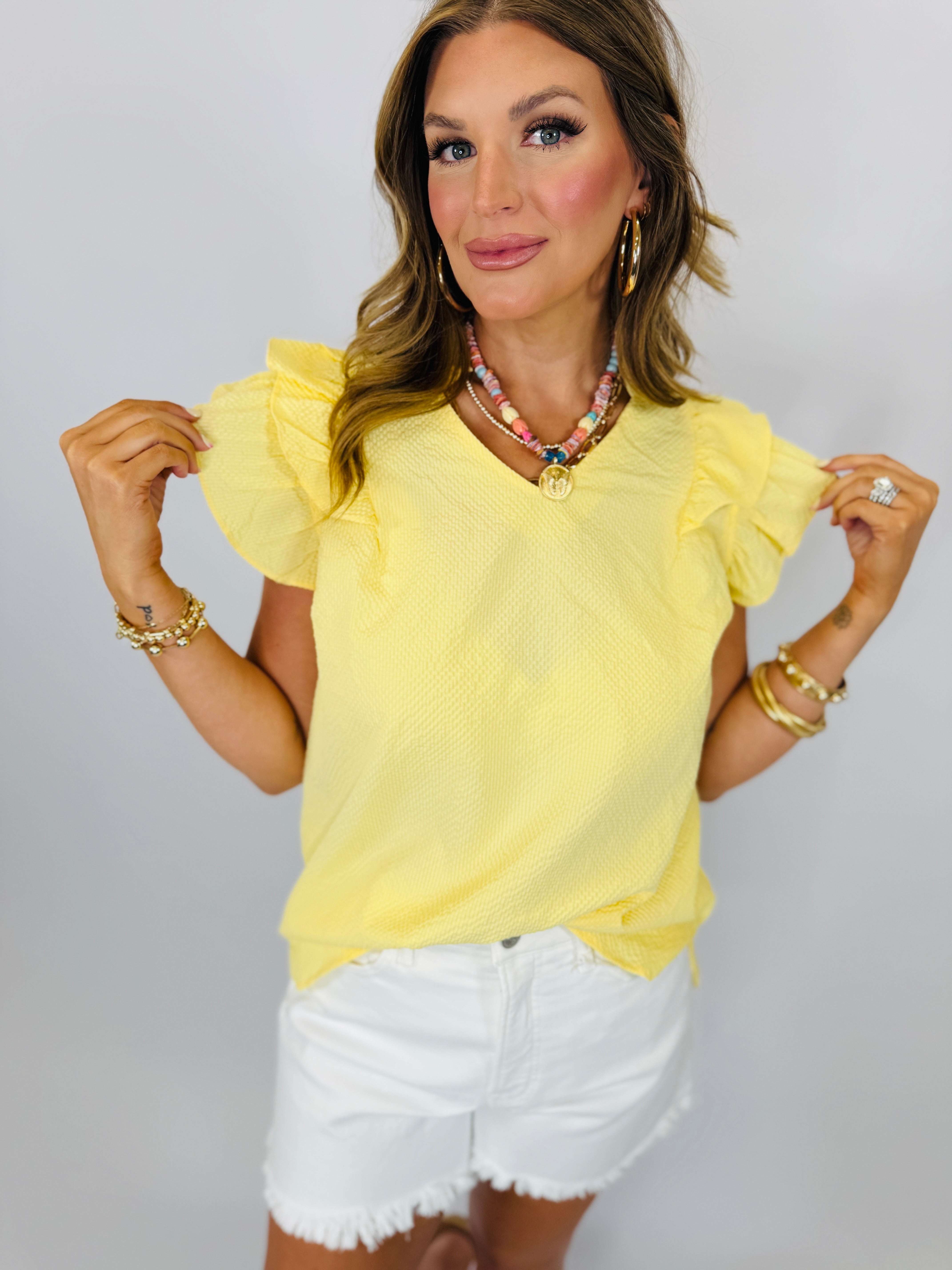 Yellow ruffled sleeve top with v-neck worn with white denim shorts and layered jewelry