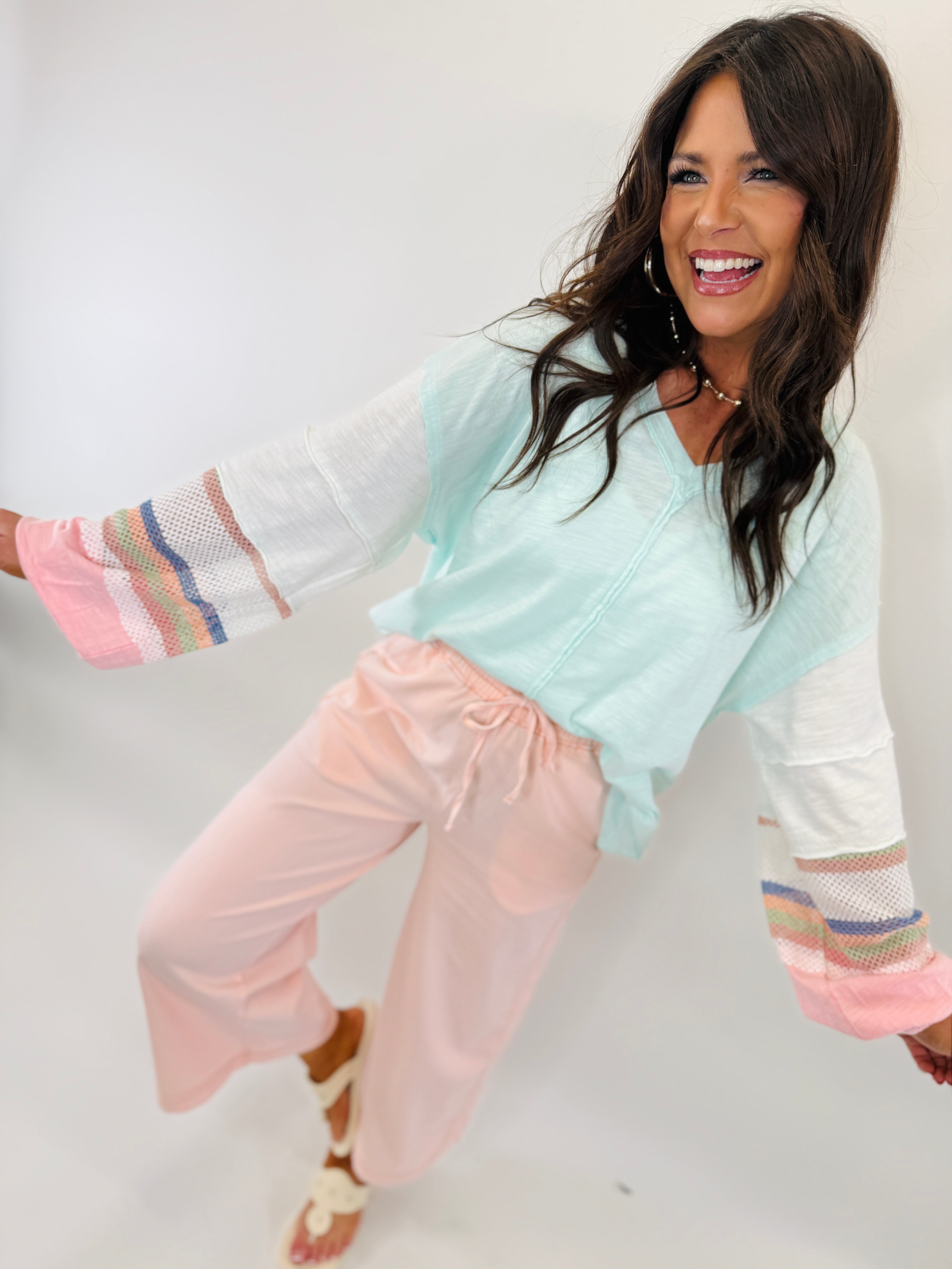 Woman wearing mint green tie-dye top with colorful striped cuffs, paired with pink sweatpants in motion.
