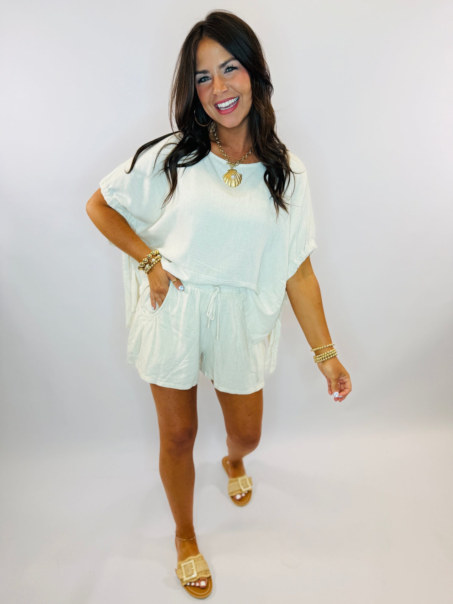 Woman wearing light blue tie-dye short-sleeve top with drawstring waist and matching shorts, styled with gold jewelry.