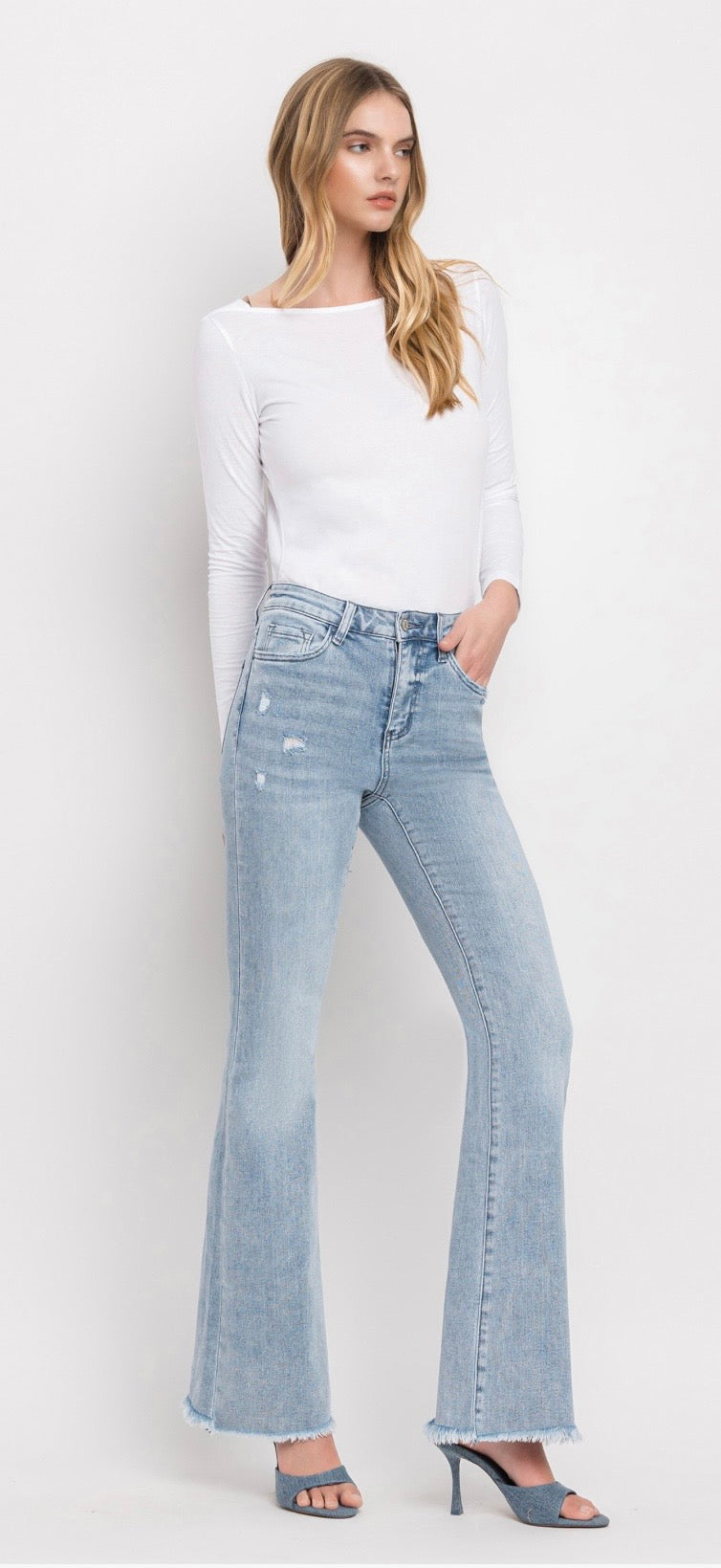 Woman wearing light blue distressed flare jeans with white long-sleeve top and denim heels