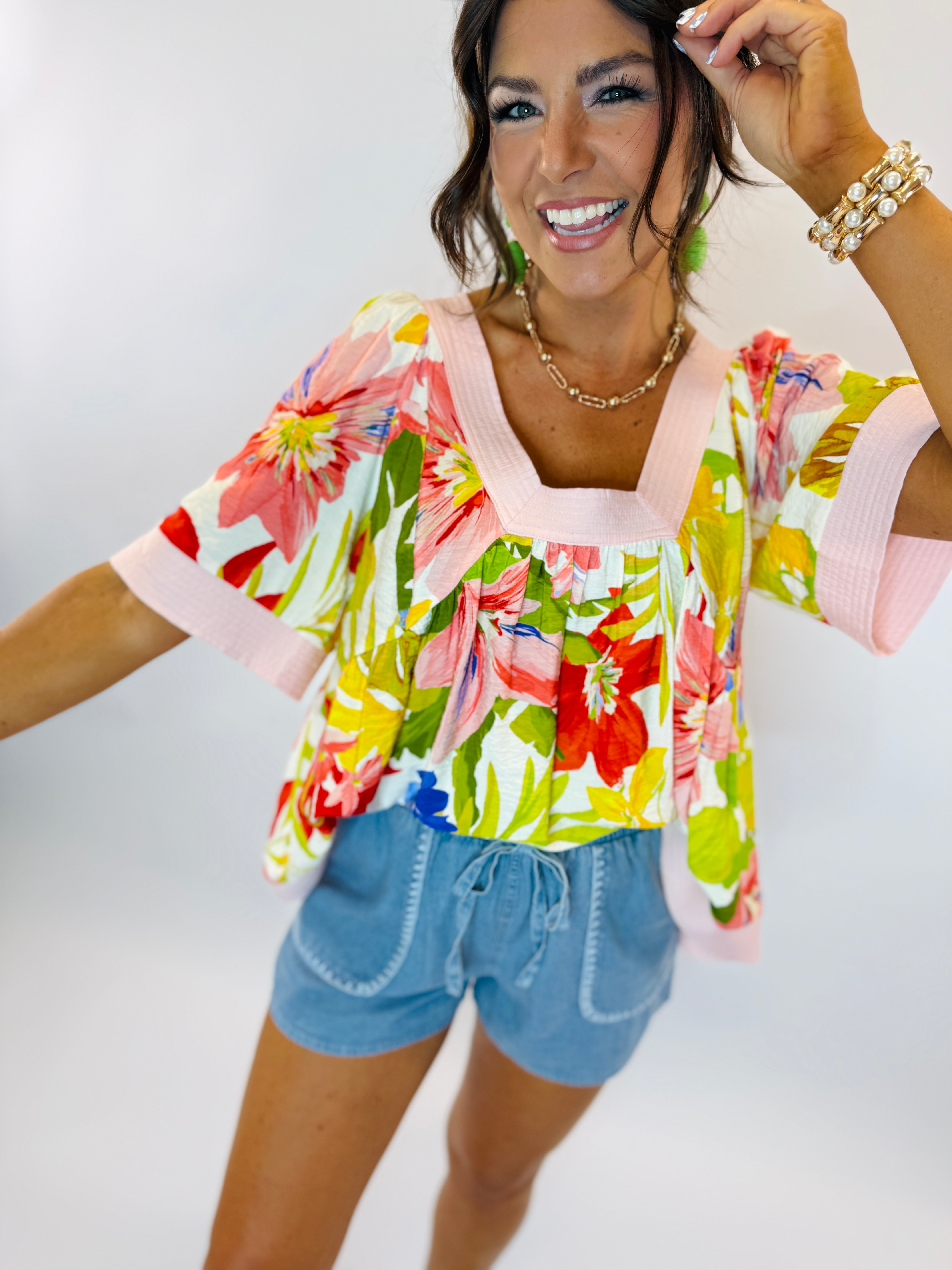 Woman wearing colorful floral Chloe top with pink trim and blue drawstring shorts, smiling and posing.