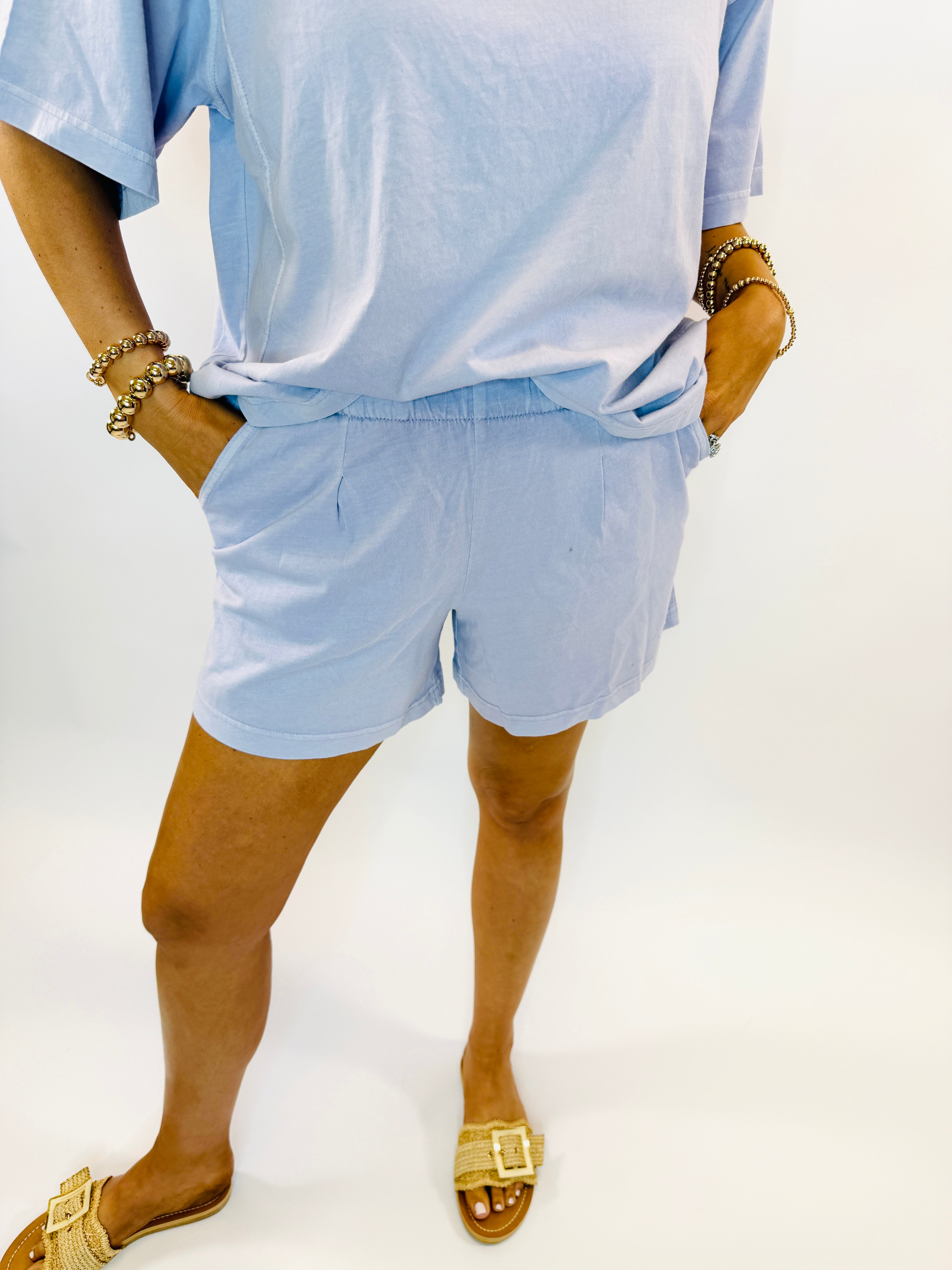 Light blue casual two-piece set with oversized t-shirt and elastic waist shorts, styled with gold jewelry and woven sandals.
