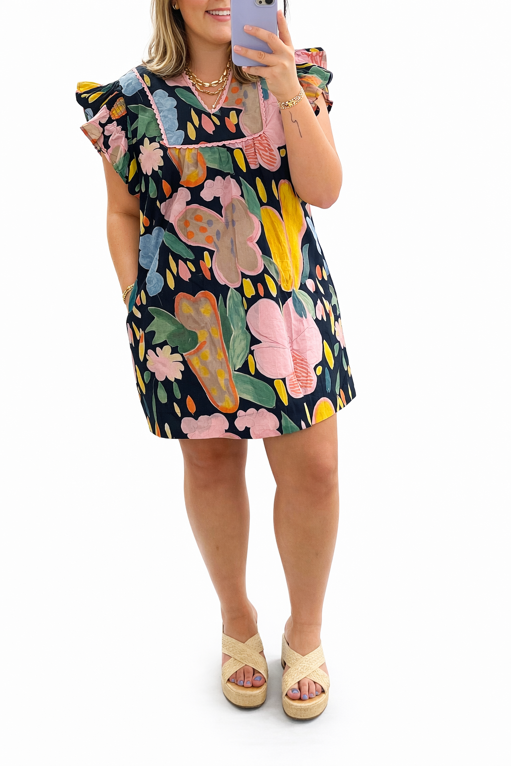 Woman wearing colorful floral Avery dress with ruffled sleeves and platform sandals, taking mirror selfie.