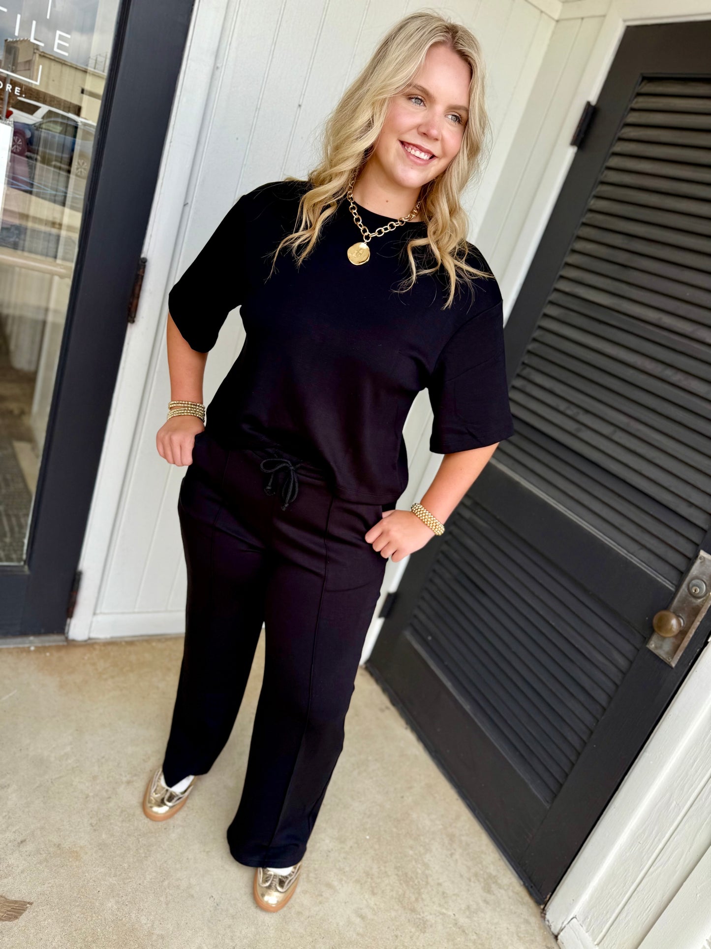 Woman wearing black coordinated set with drawstring bottoms and half-sleeve top, accessorized with gold jewelry