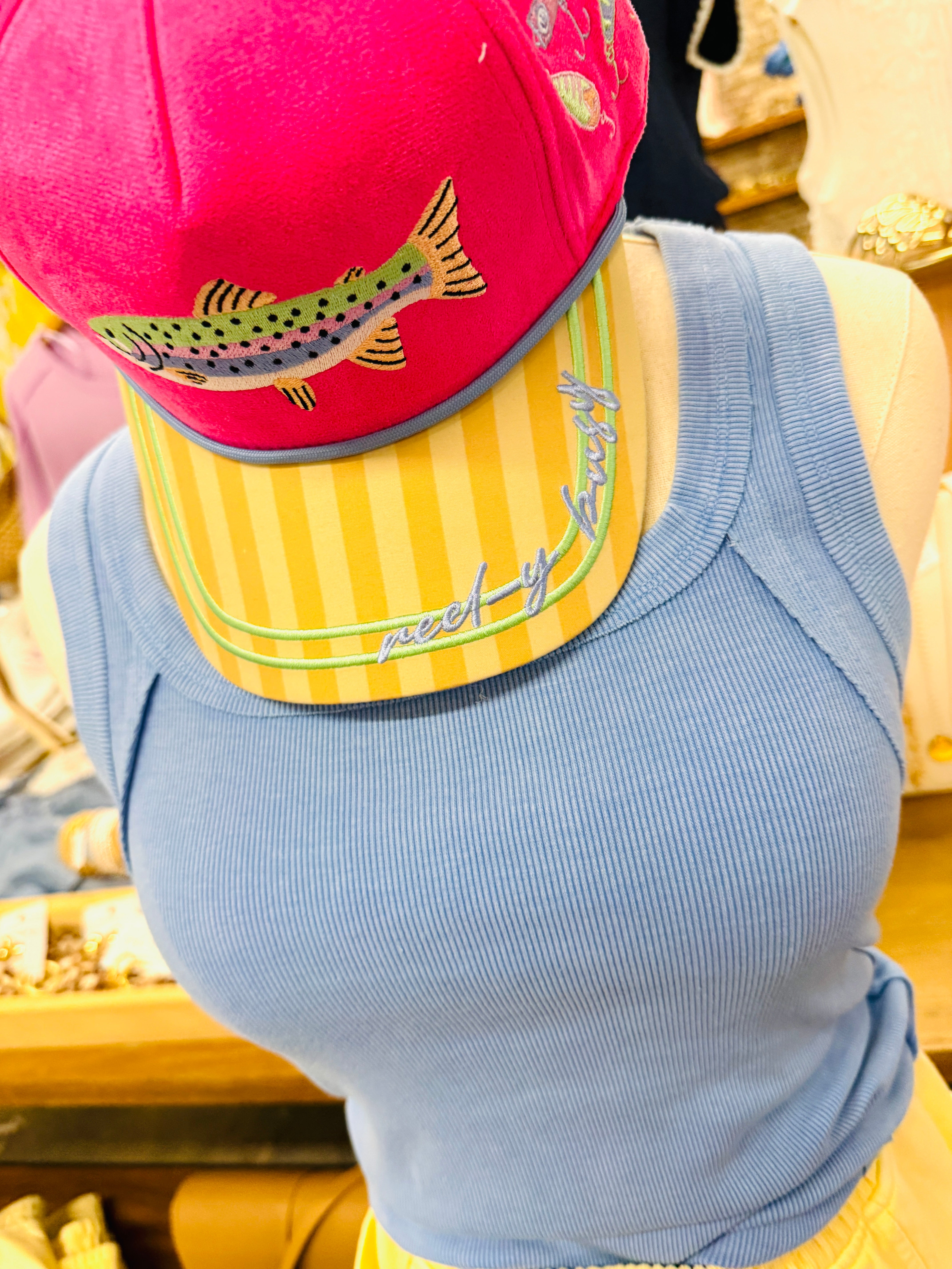 Hot pink snapback hat with embroidered rainbow trout, yellow striped brim, and "Reel-y Busy" script text.