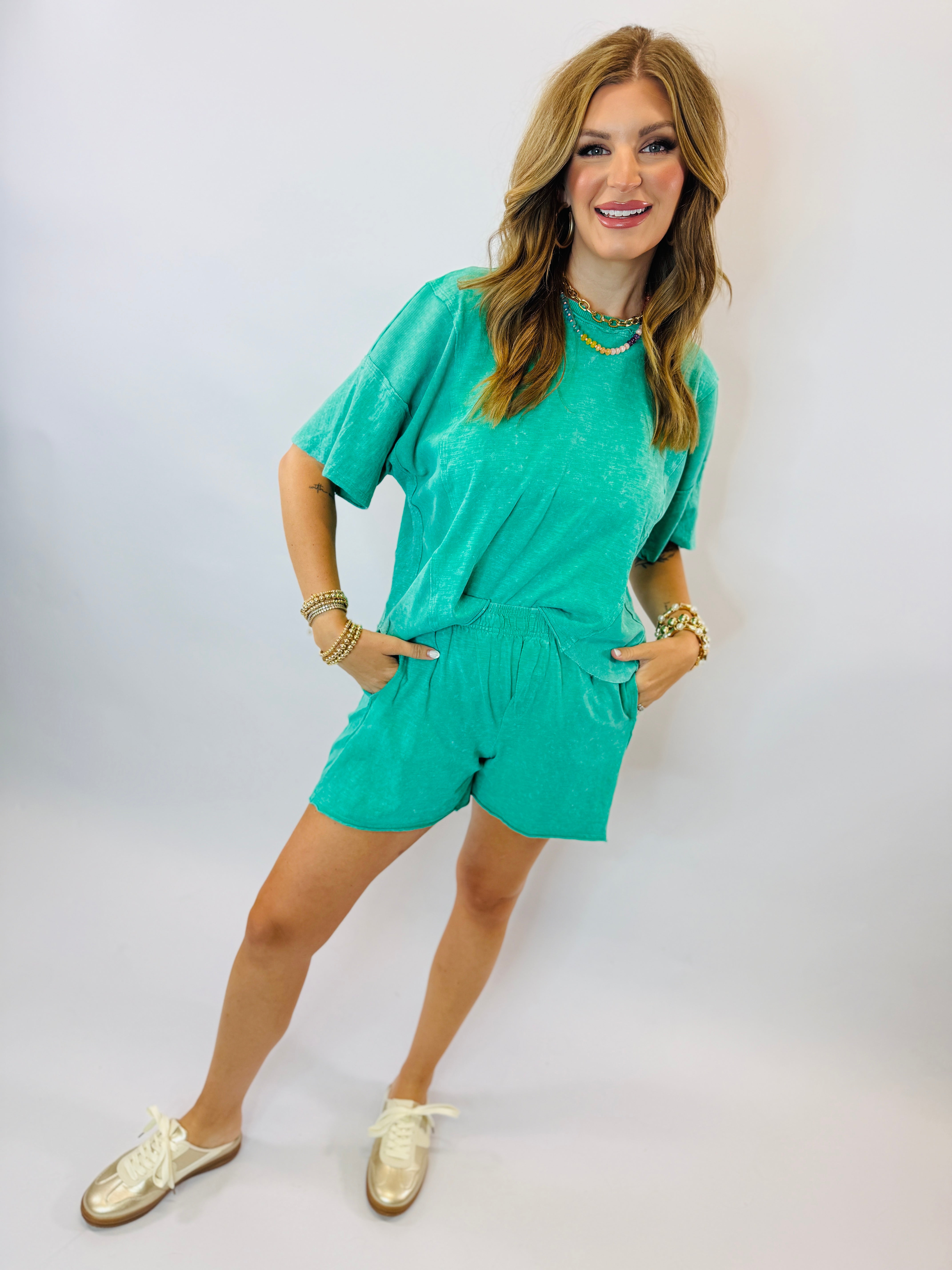 Woman wearing turquoise short-sleeve top and matching shorts set with gold jewelry and shoes
